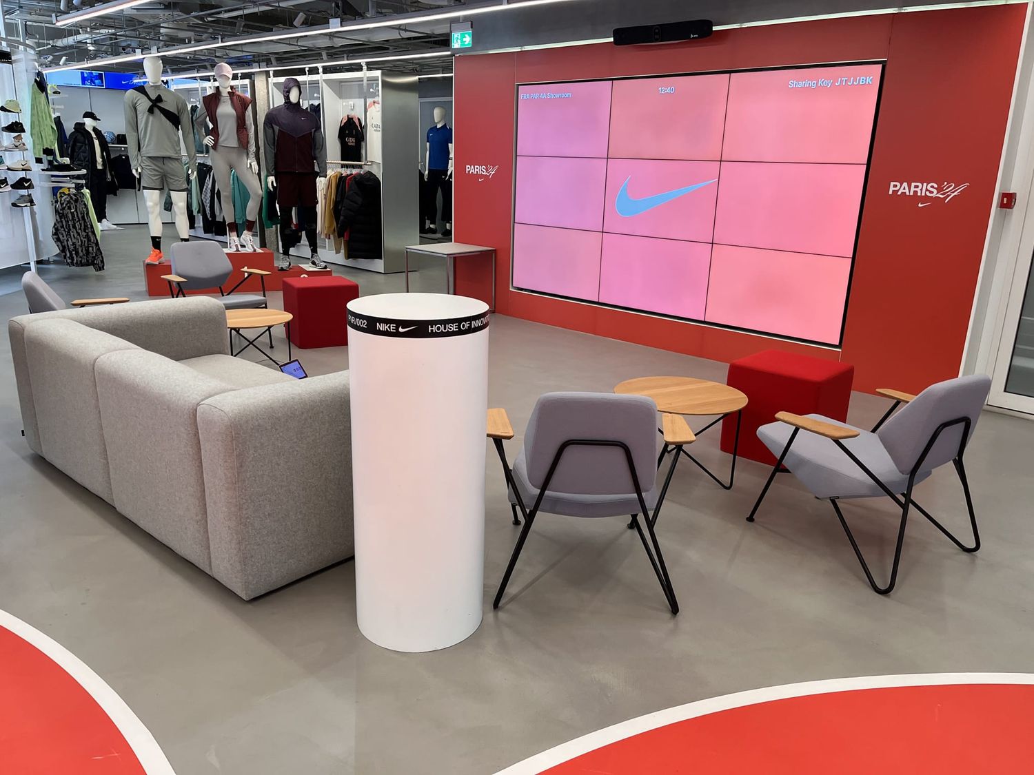 Nike Paris store interior with red walls, lounge seating, and large branded display screen.
