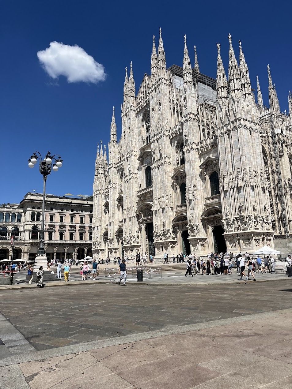 Milan Cathedral Duomo di Milano with Gothic spires under blue sky, tourists in the piazza.