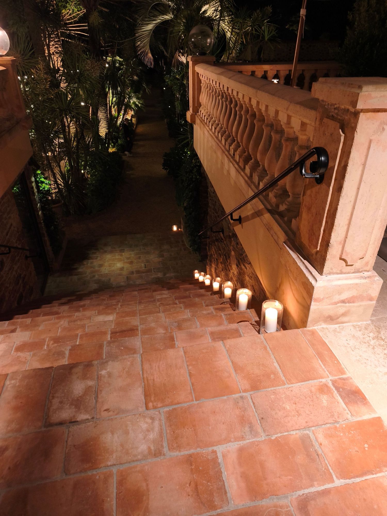 Candlelit terracotta staircase at night with glowing pillar candles lining stone steps in lush garden setting.