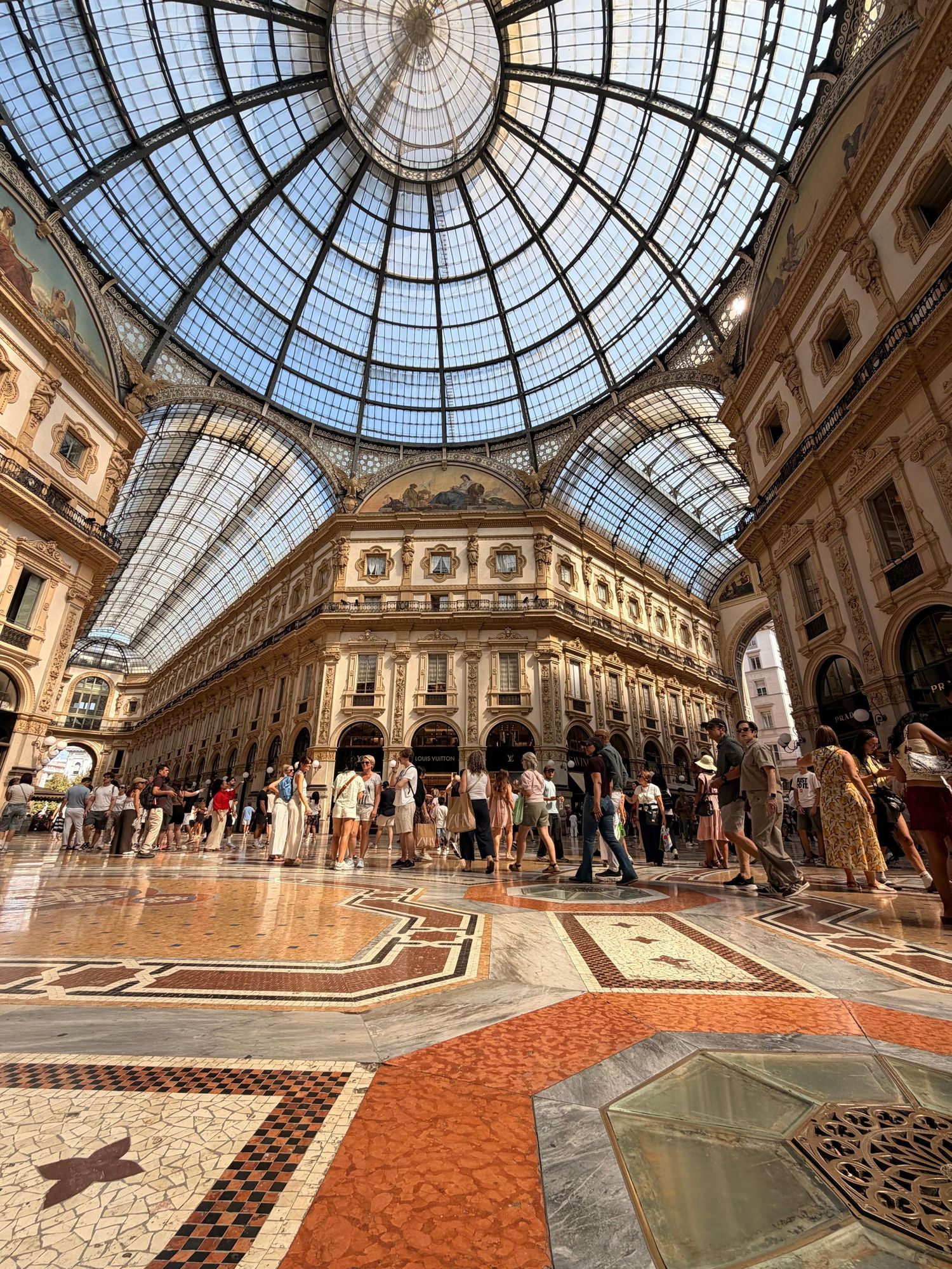 Galleria Vittorio Emanuele II Milan interior with stunning glass dome ceiling and mosaic floors.