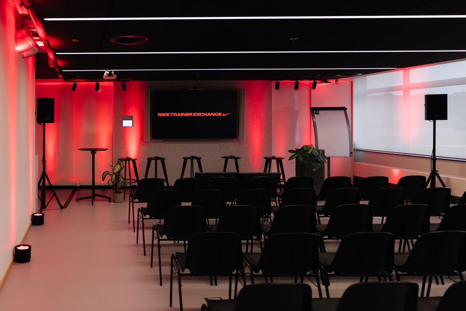 Empty conference room with red accent lighting, rows of chairs, and a Nike Training Exchange projection screen.