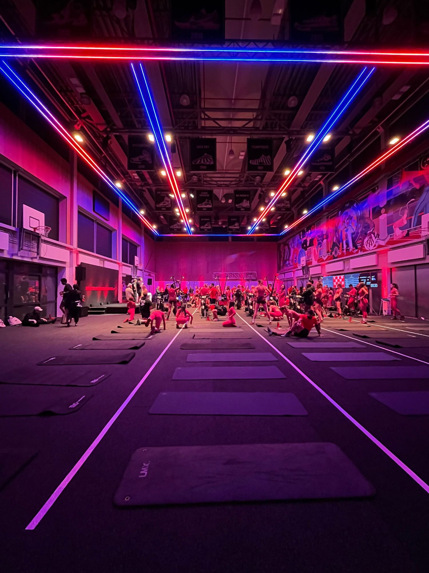 Large fitness studio with neon red and blue lights illuminating rows of exercise mats during a group workout class.