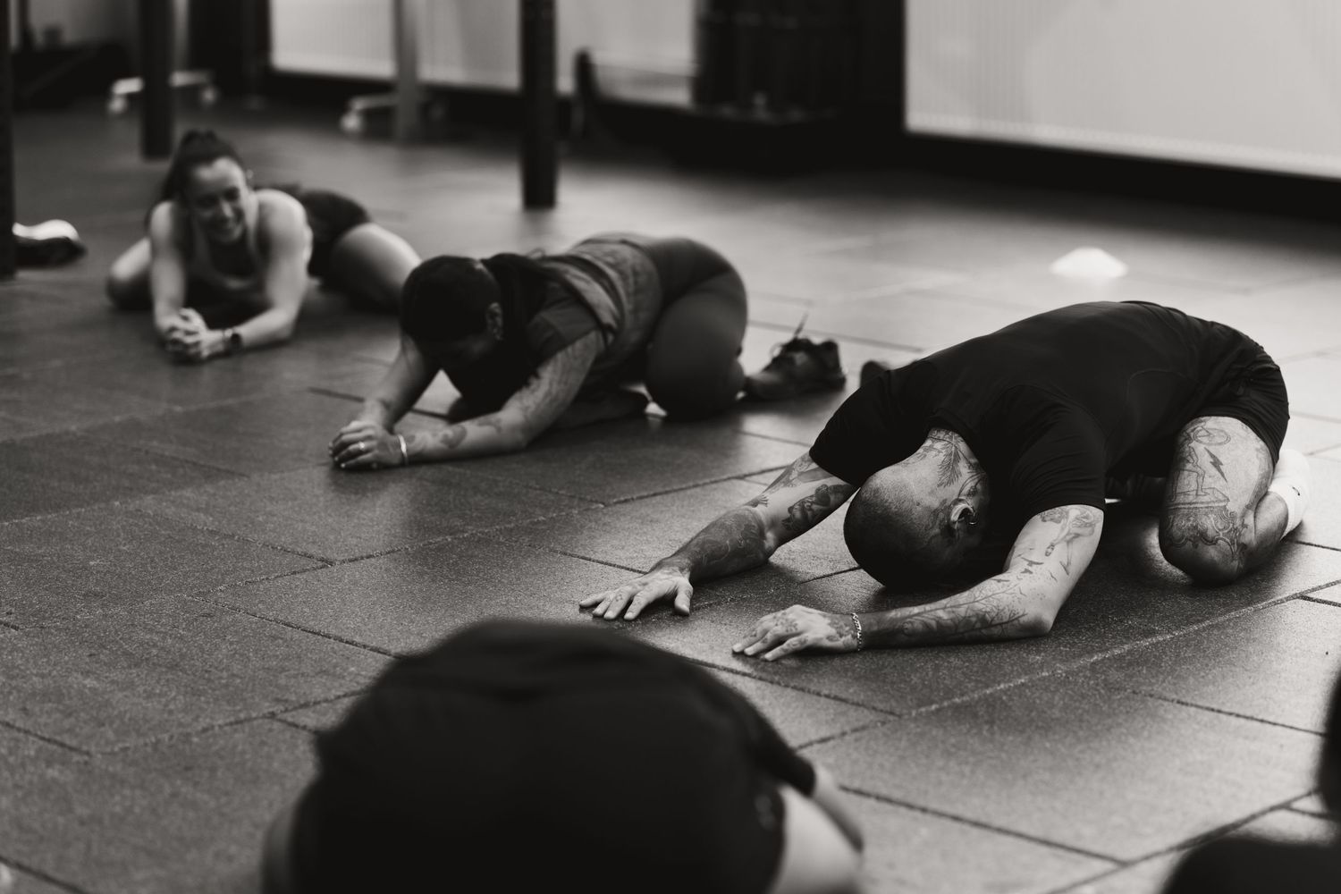 Black and white photo of people stretching on gym floor during a fitness class session.