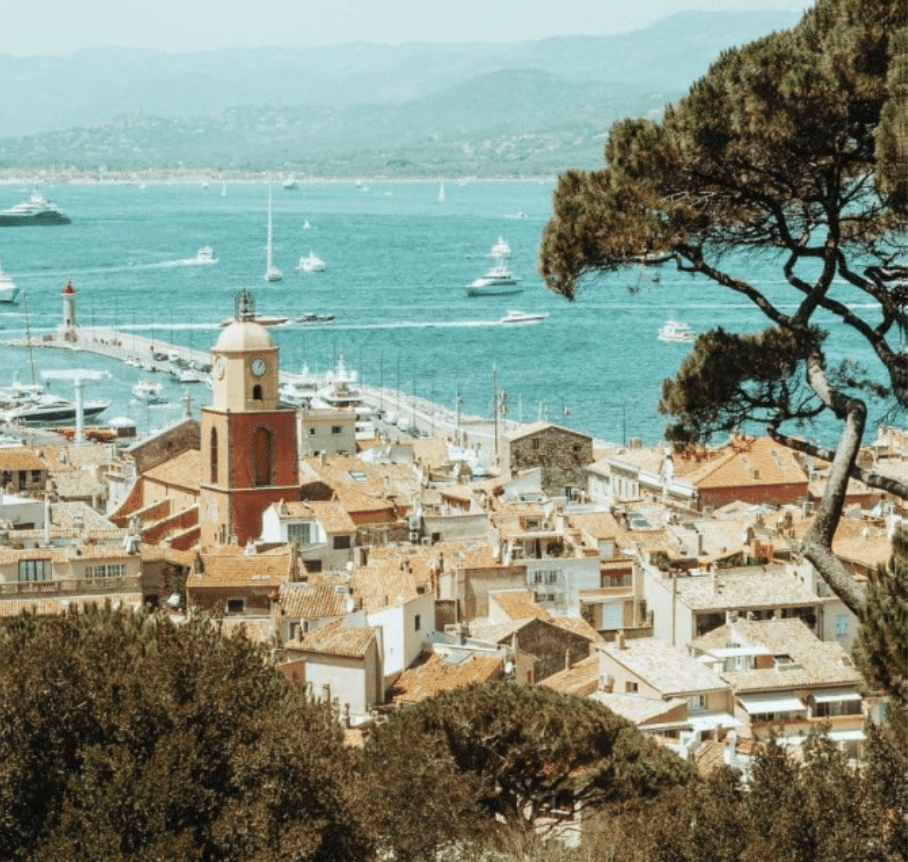 Aerial view of Saint-Tropez old town with red bell tower, terracotta rooftops, and yacht-filled harbor.