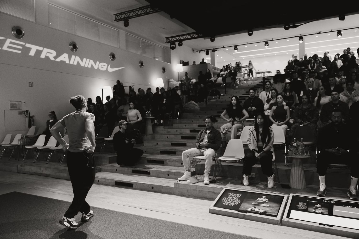 Black and white photo of a Nike Training event with an instructor leading a session for an audience seated on stadium steps.