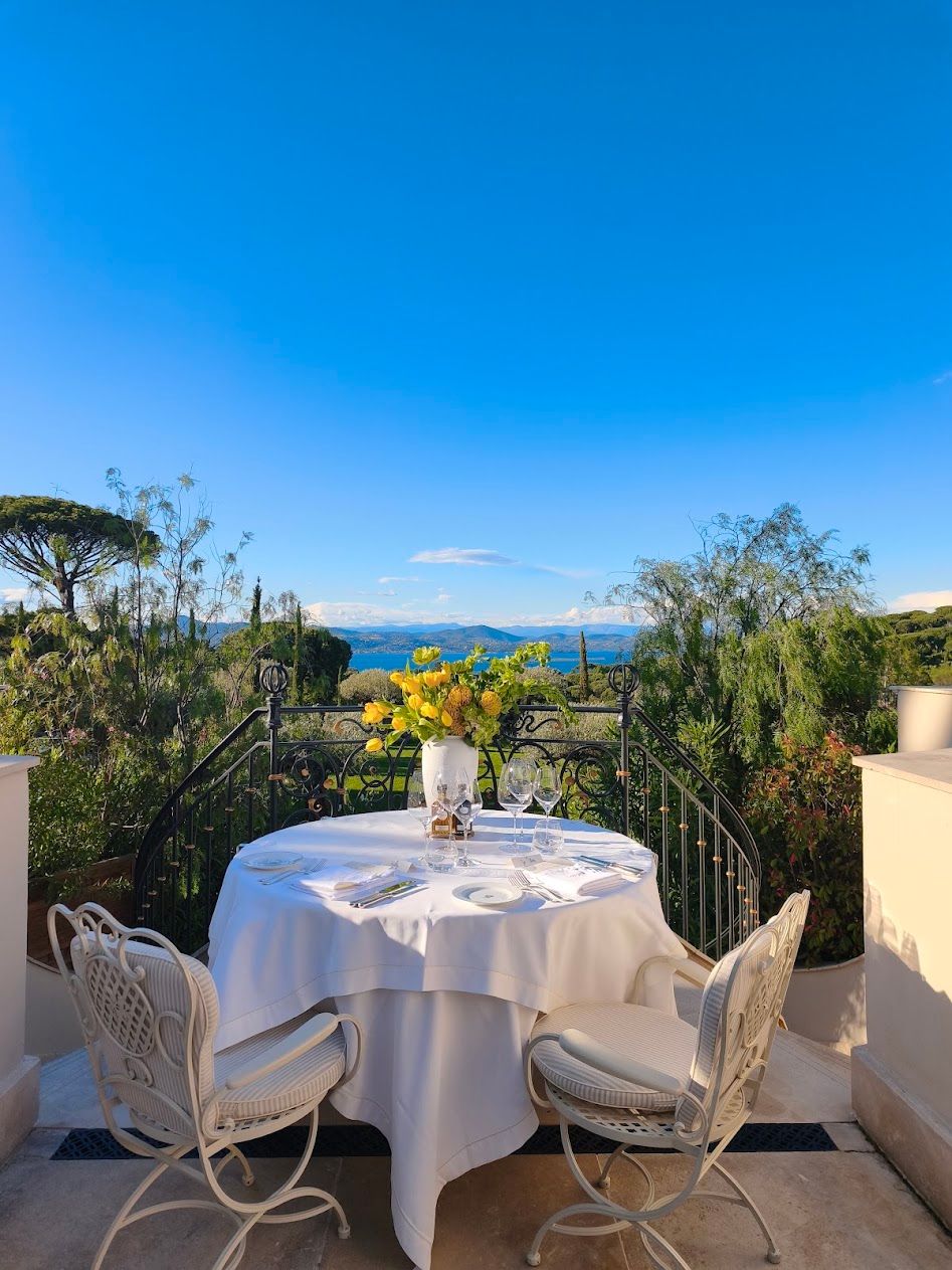 Romantic terrace table set for two with yellow blooms overlooking a stunning coastline.