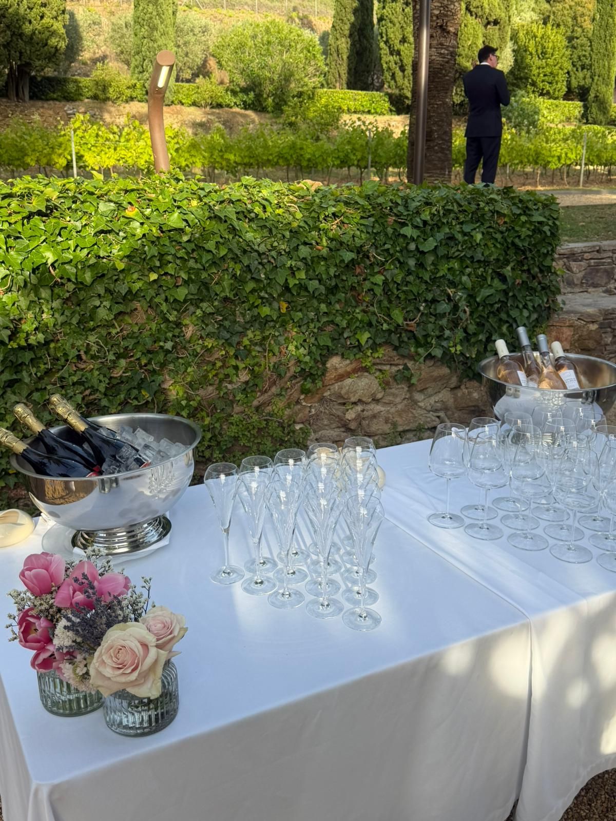 Elegant champagne bar with flutes, ice buckets, and pink floral arrangements in a garden setting.