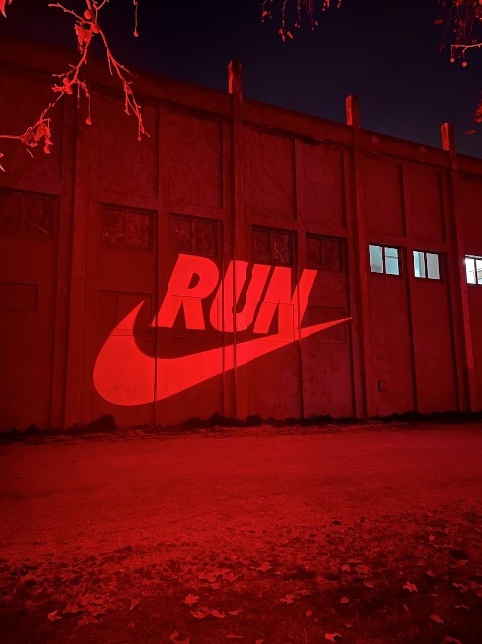 Bold red Nike RUN swoosh mural illuminated on concrete warehouse wall after dark.