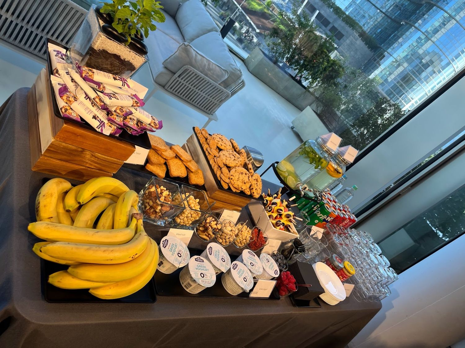 Luxury hotel breakfast buffet spread with bananas, pastries, granola, and fresh fruit by large window.