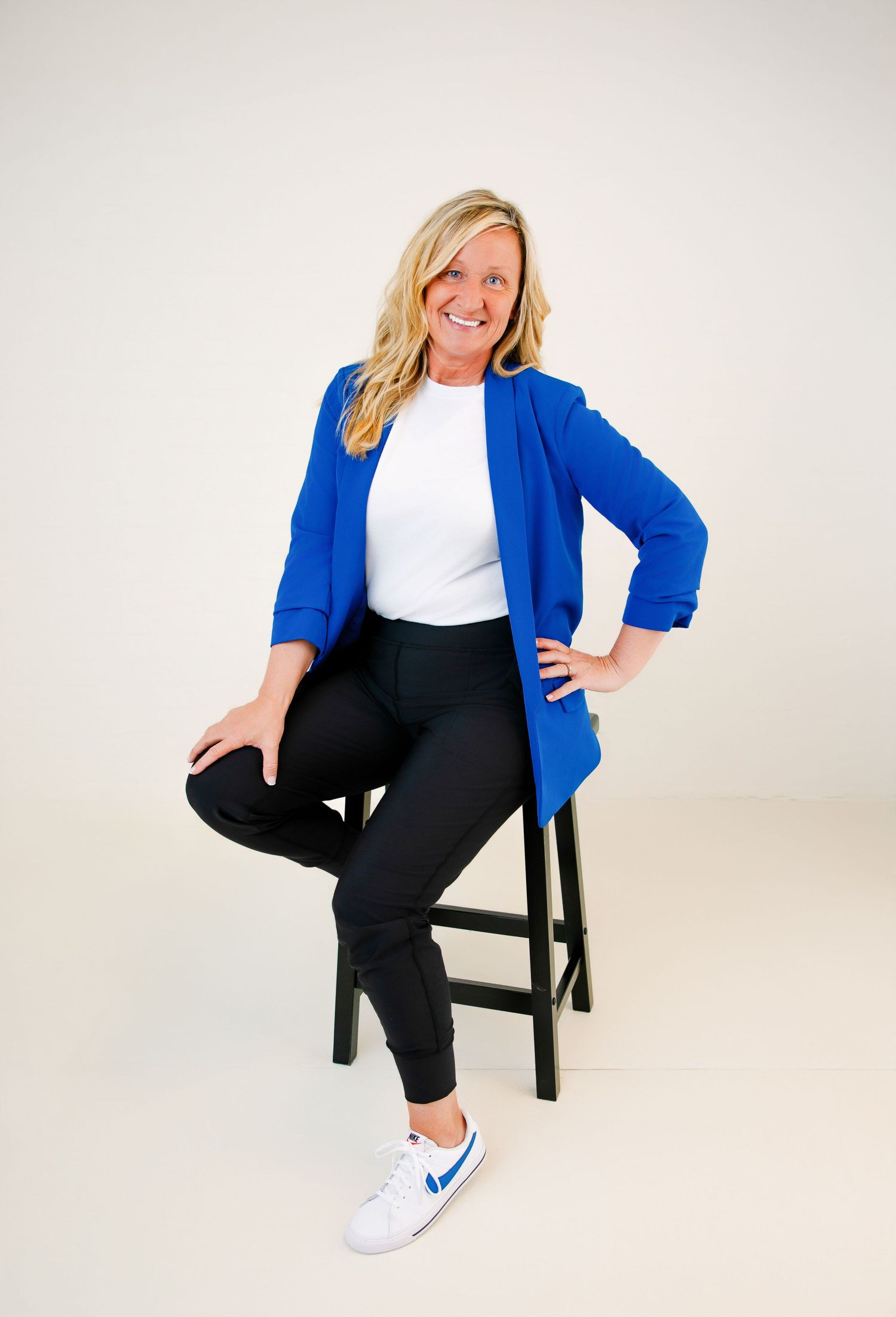 Photo of a Business Branding photographer sitting on a black stool wearing a royal blue blazer and black pants.