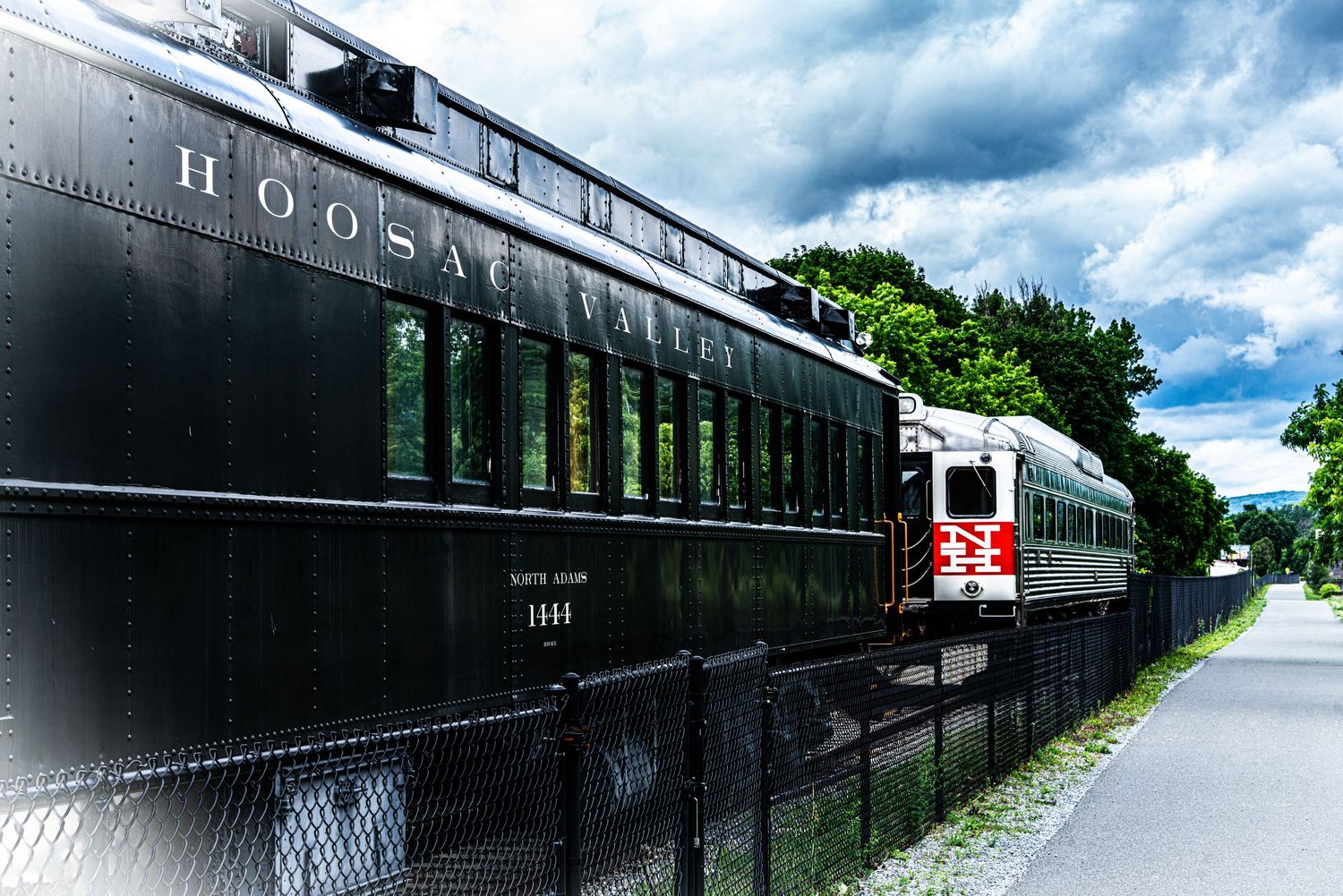 Vintage Hoosac black train car alongside a modern passenger train on tracks.