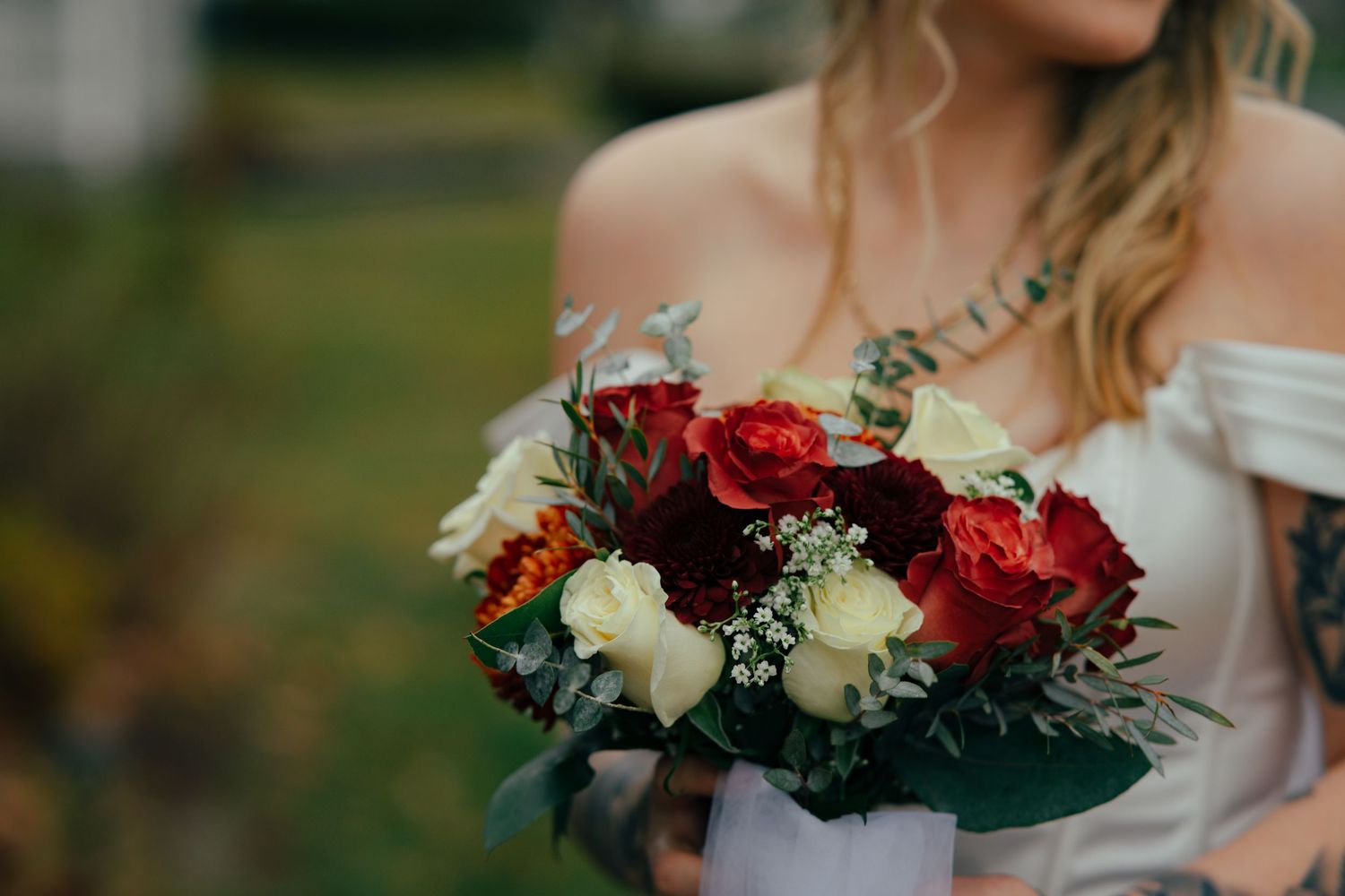 Bride holding a bouquet of red, white, and burgundy roses with greenery.