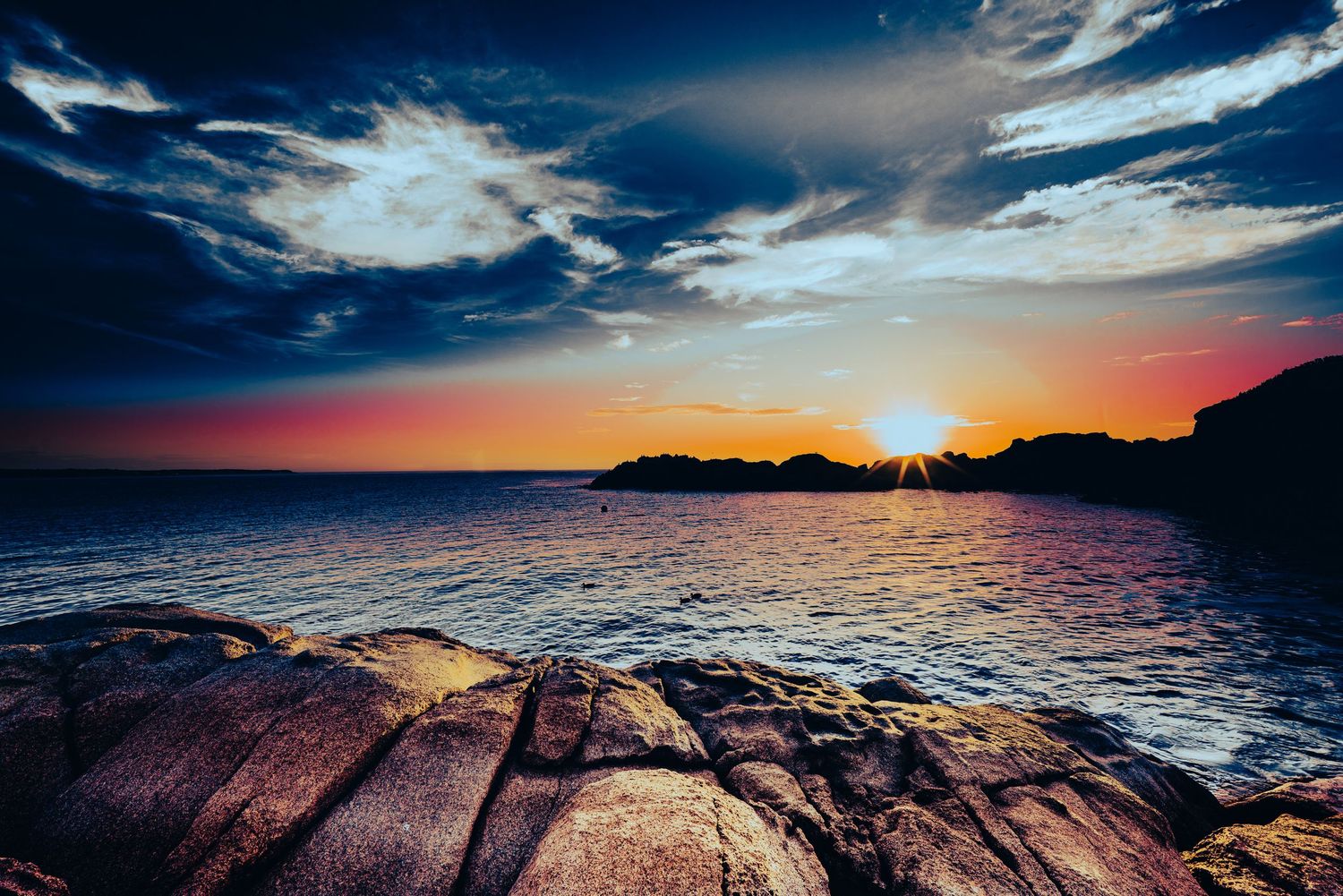 Dramatic sunset over rocky ocean coastline with vibrant blue cloudy sky.