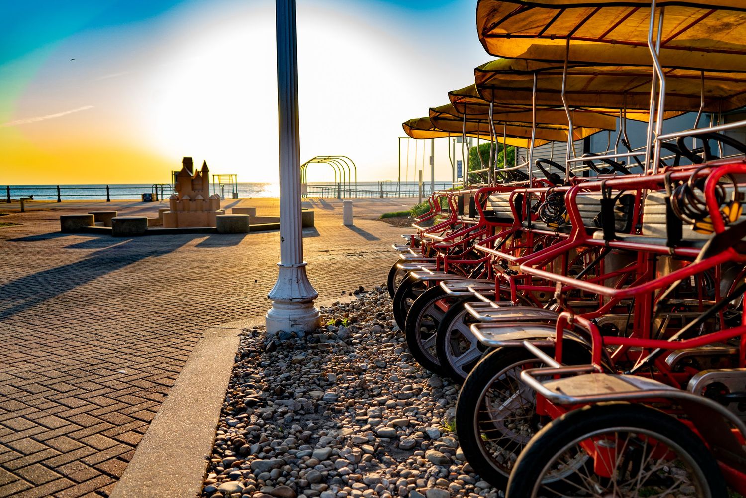 Red pedal bikes parked along a beachside promenade at golden sunset.
