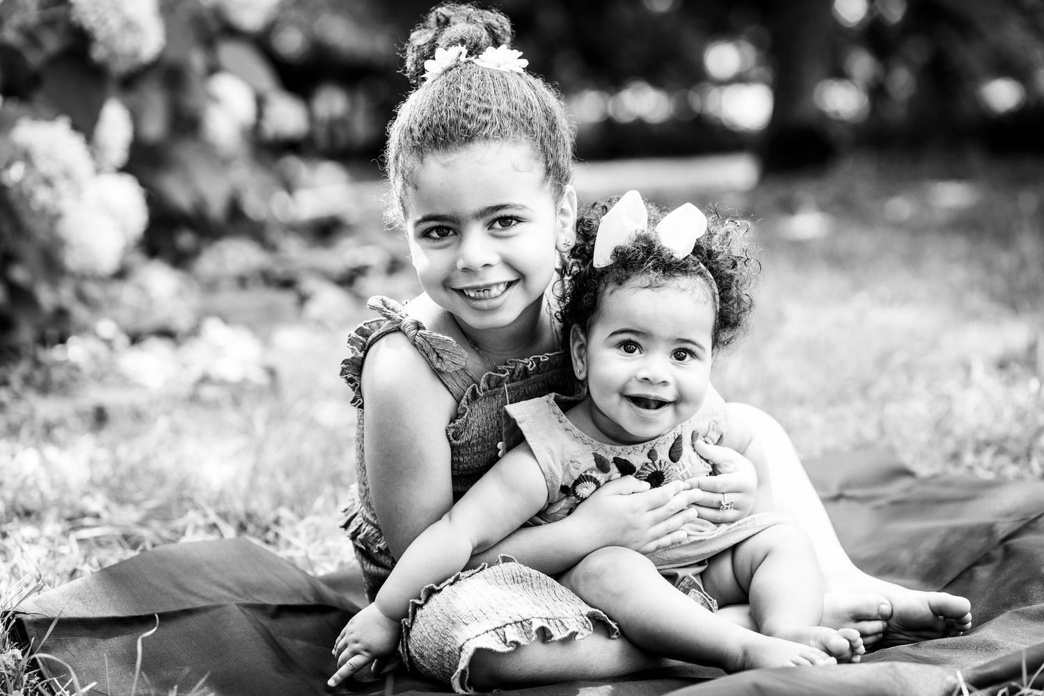 Black and white portrait of two smiling young sisters sitting together outdoors on a blanket.