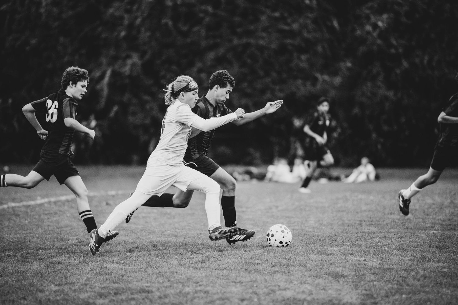 Black and white photo of youth soccer players sprinting and competing for the ball on a grass field.