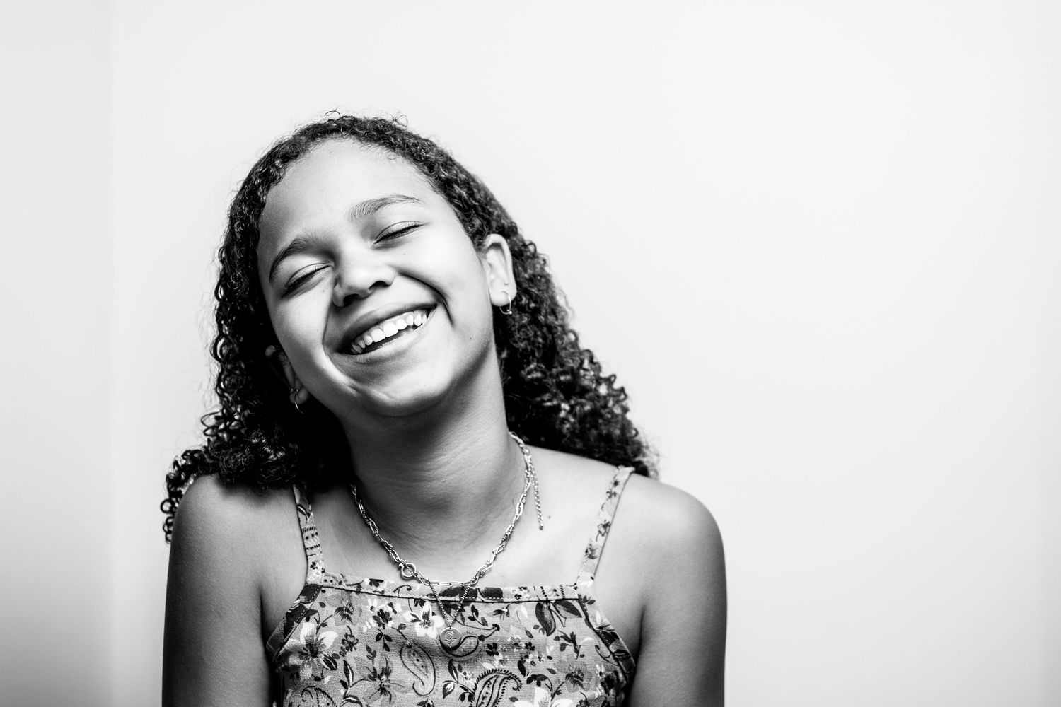 Happy young girl with curly hair laughing with eyes closed in a black and white portrait photo.