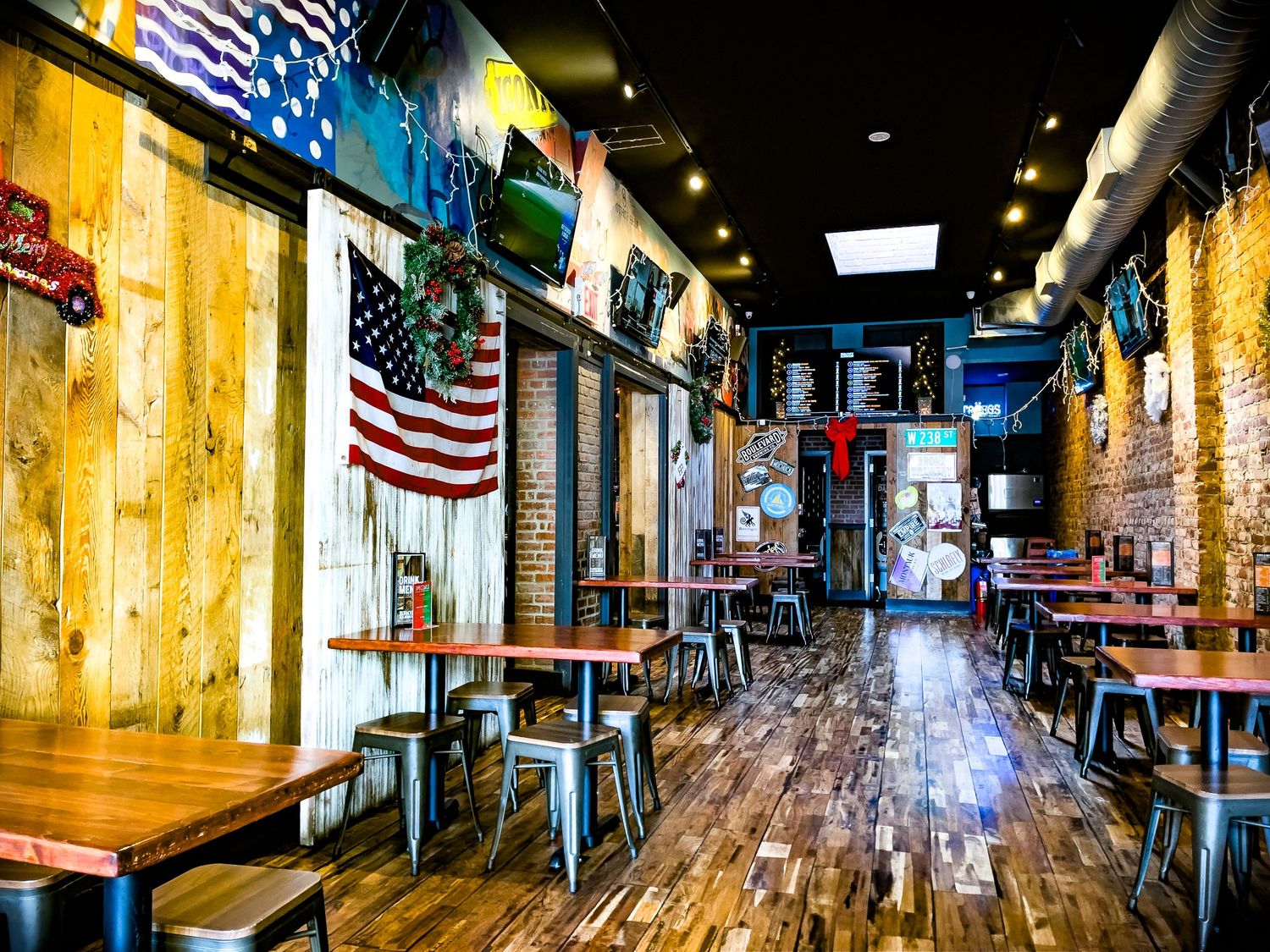 Rustic American bar interior with wood plank walls, US flag decor, metal stools, and hardwood floors.