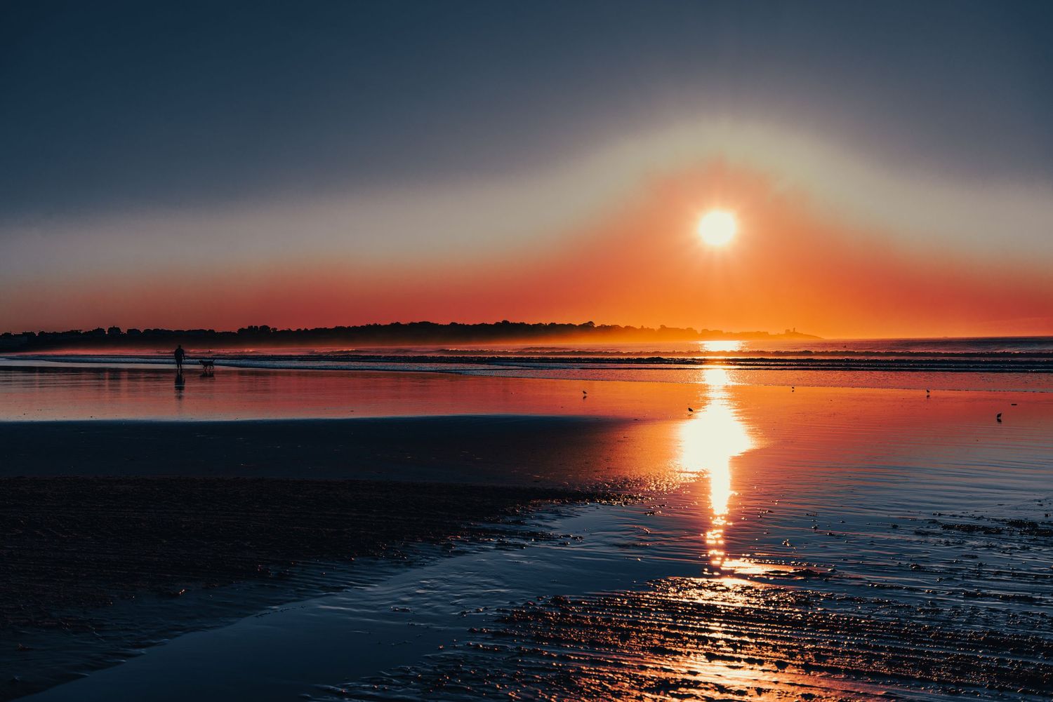 Stunning orange sunset reflecting on a calm, shallow tidal beach.
