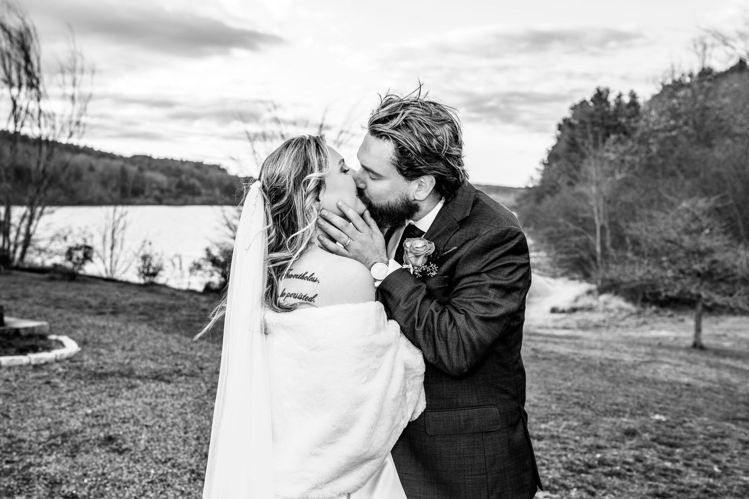 Black and white photo of a bride and groom sharing a romantic kiss outdoors on their wedding day.