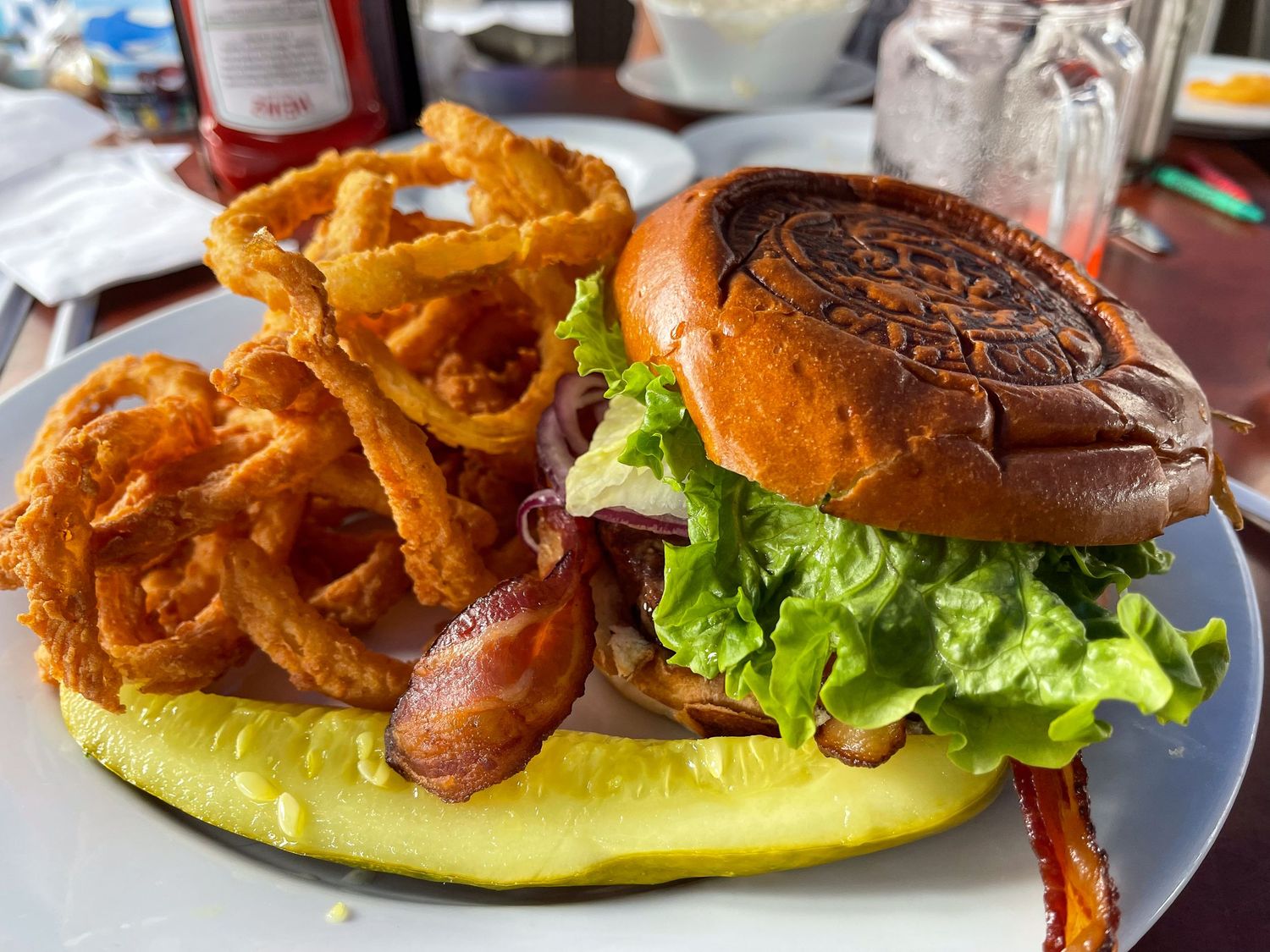 A juicy burger with lettuce, bacon, and toppings served with crispy onion rings on a white plate.