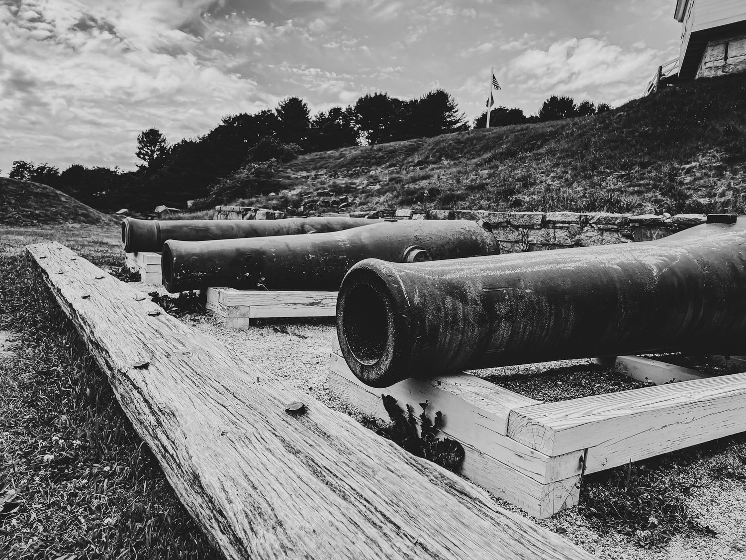 Black and white photo of vintage iron cannons resting on wooden beams at an outdoor historic site.