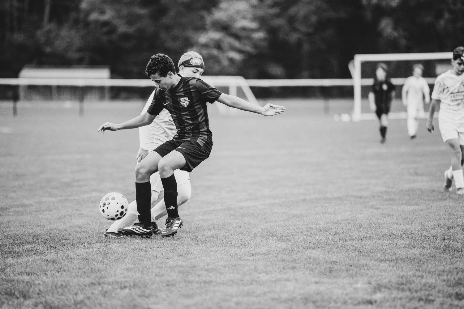 Black and white action shot of youth soccer players competing for the ball during a match.