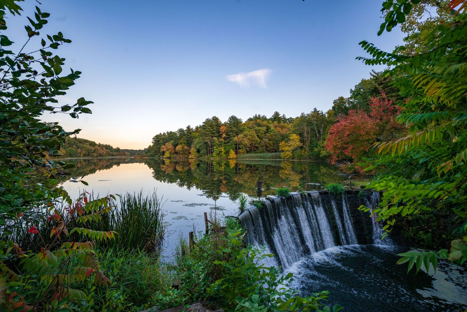 Scenic autumn waterfall flowing into a calm lake surrounded by colorful foliage at sunset.