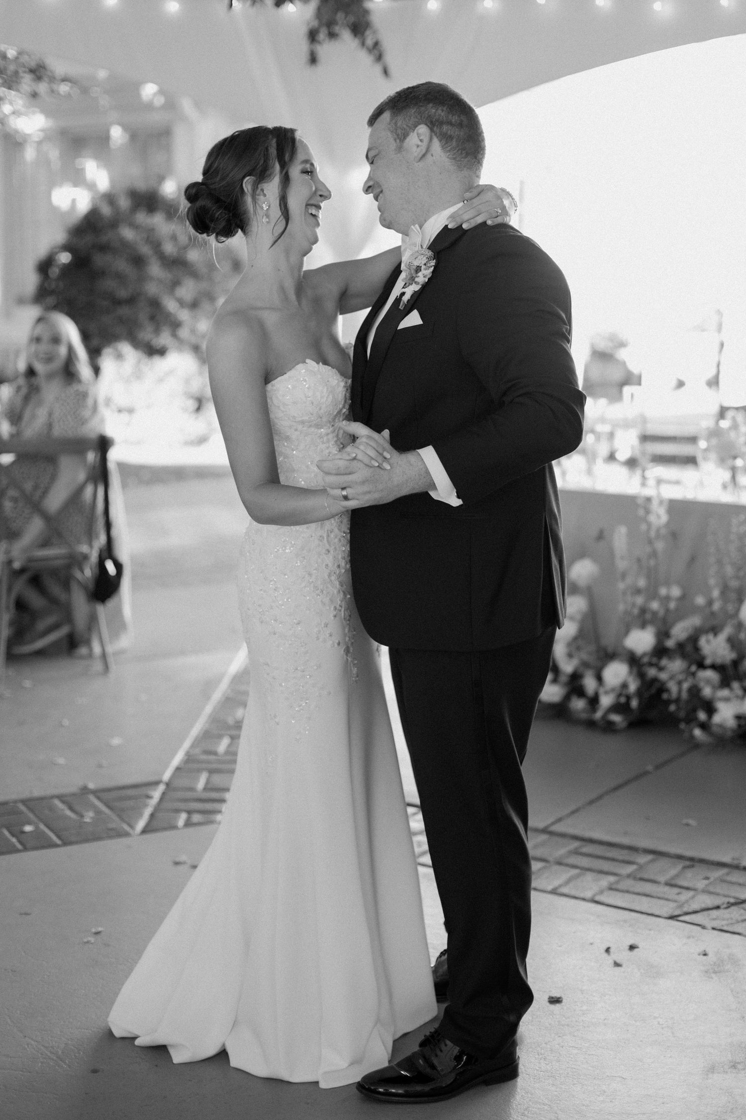 A newlywed couple shares their first dance under twinkling lights at an outdoor wedding reception.