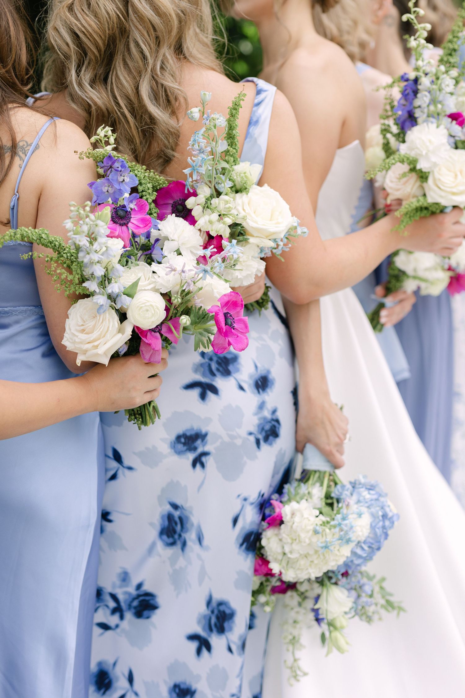 Bridesmaids holding colorful spring bouquets wear light blue floral dresses at an elegant wedding ceremony.