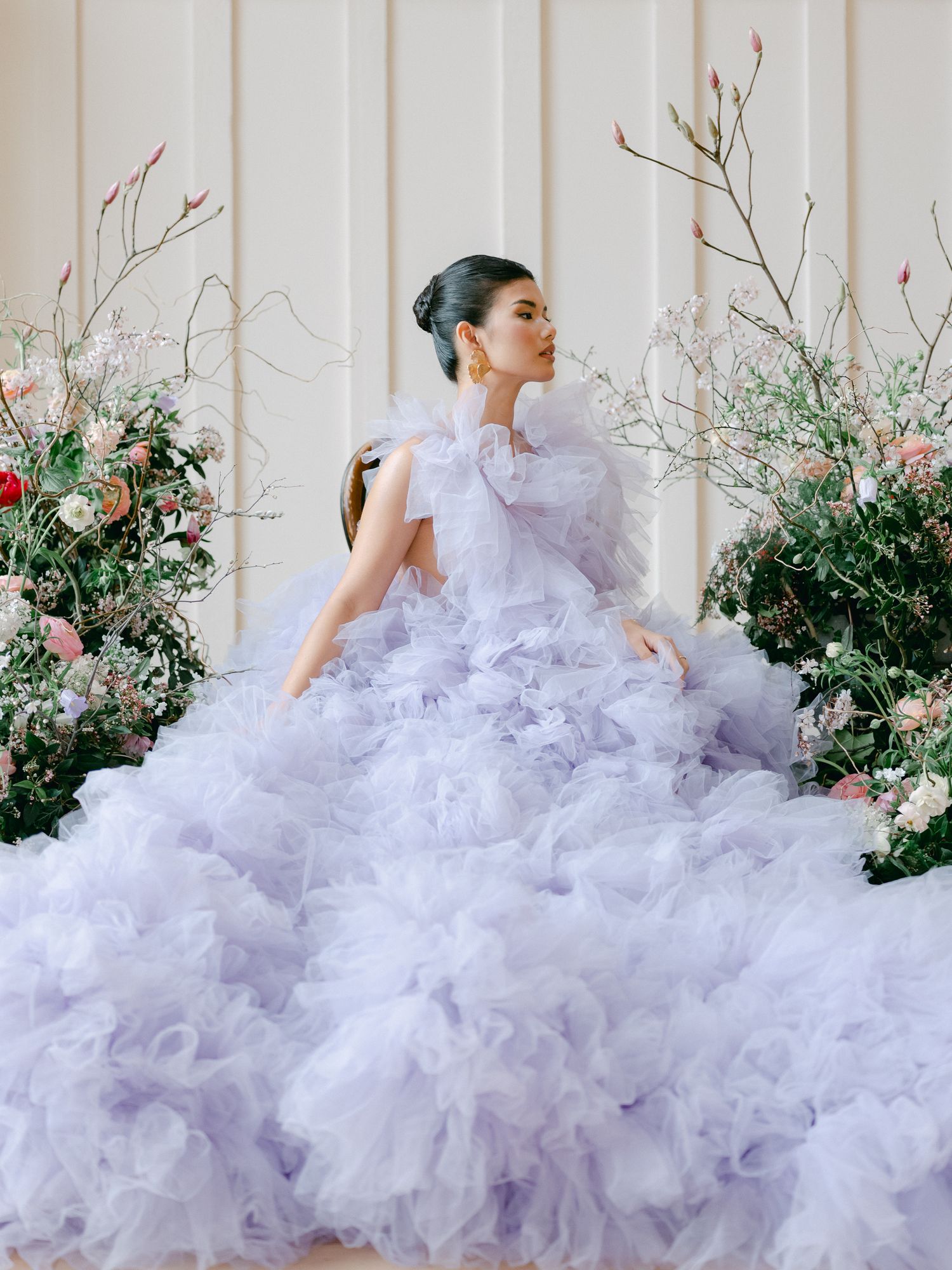 A figure in a voluminous white tulle gown poses gracefully among flowering bushes in a romantic garden setting.
