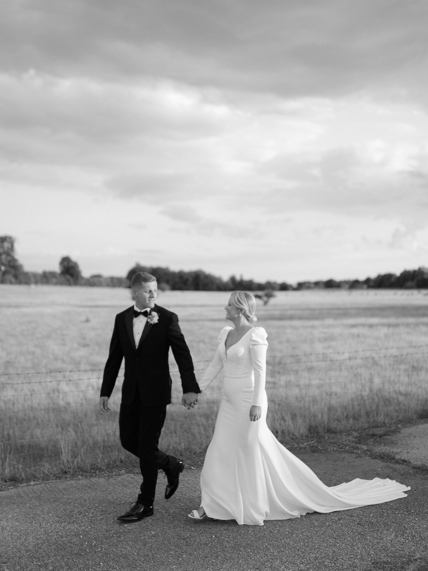 A couple in wedding attire runs playfully through a misty field in black and white photography.