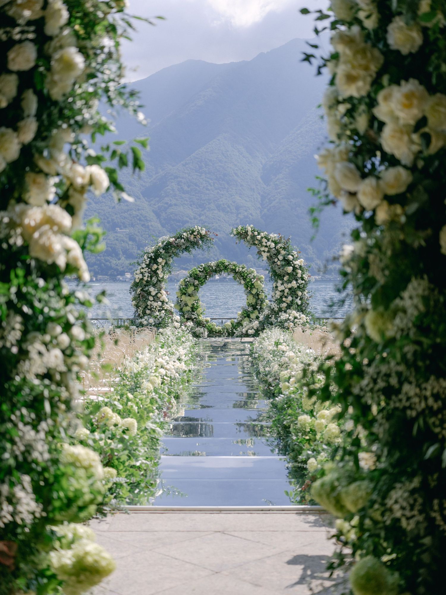 Romantic floral wedding arch with white roses framing mountain view in destination ceremony setting. Lake Como.