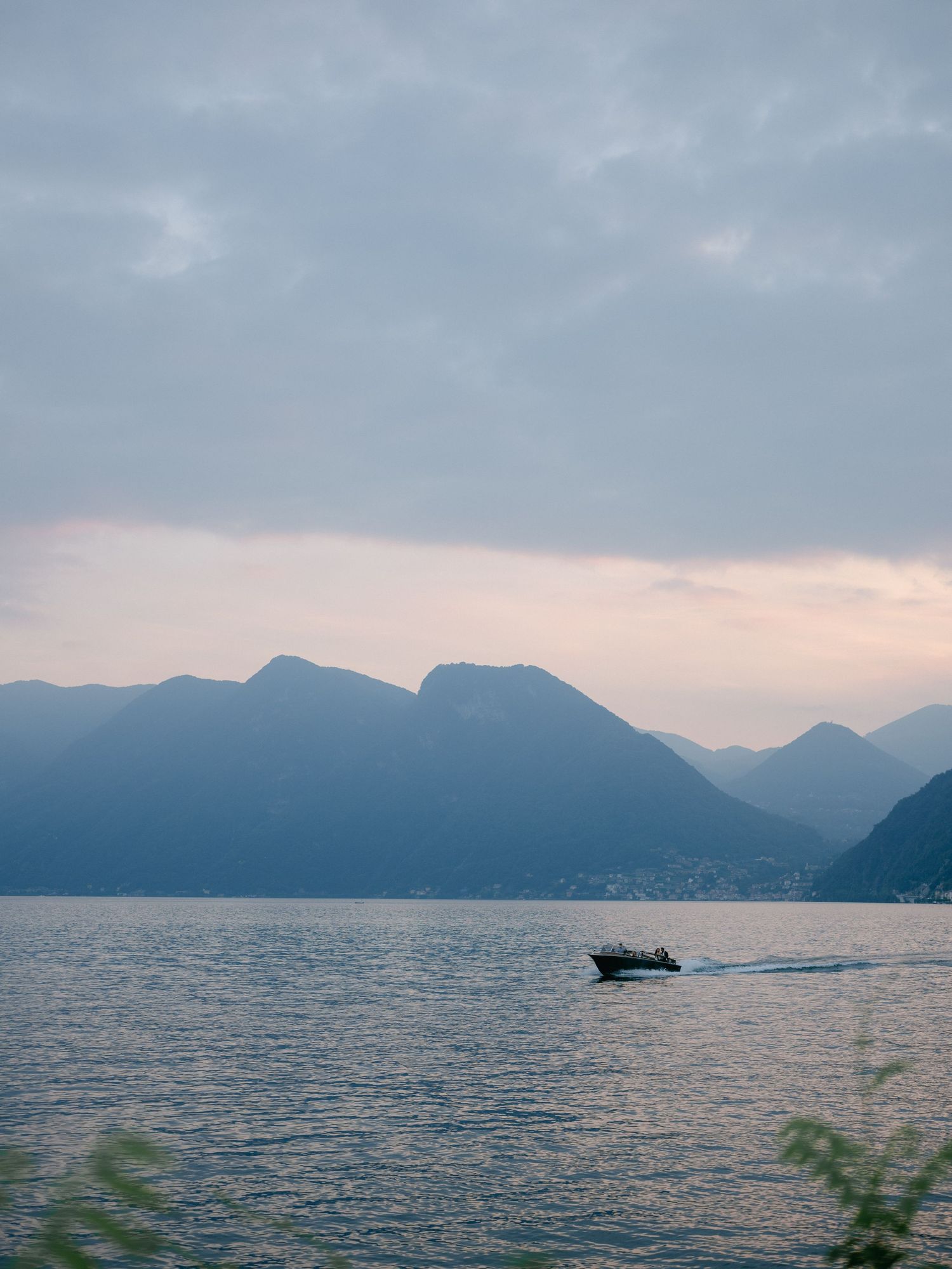 A panoramic view of misty mountains and calm waters at dusk with silhouetted peaks against a moody sky.