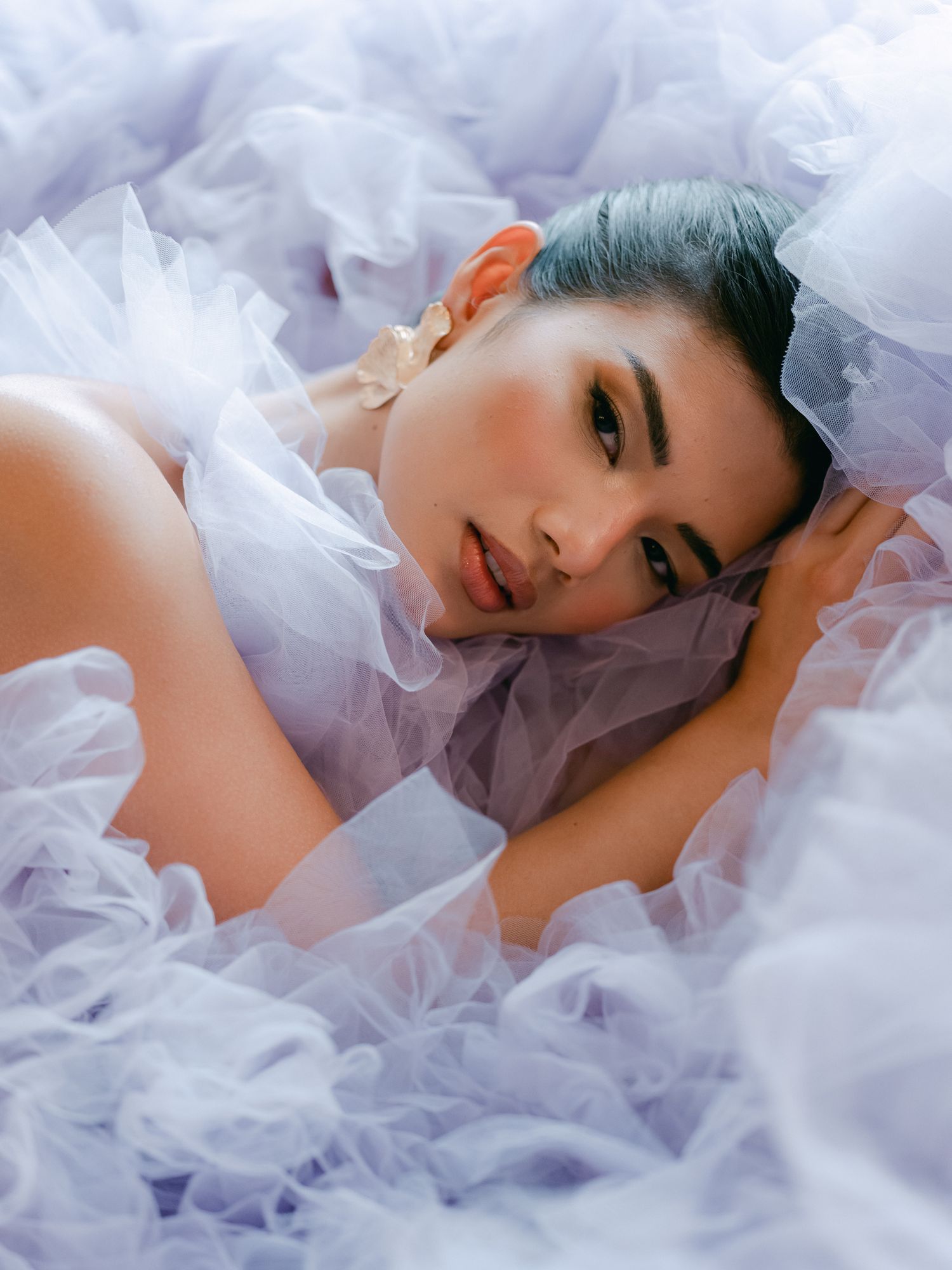 A dreamy portrait with soft white tulle fabric surrounding a figure with blue-tinted hair in an ethereal pose.