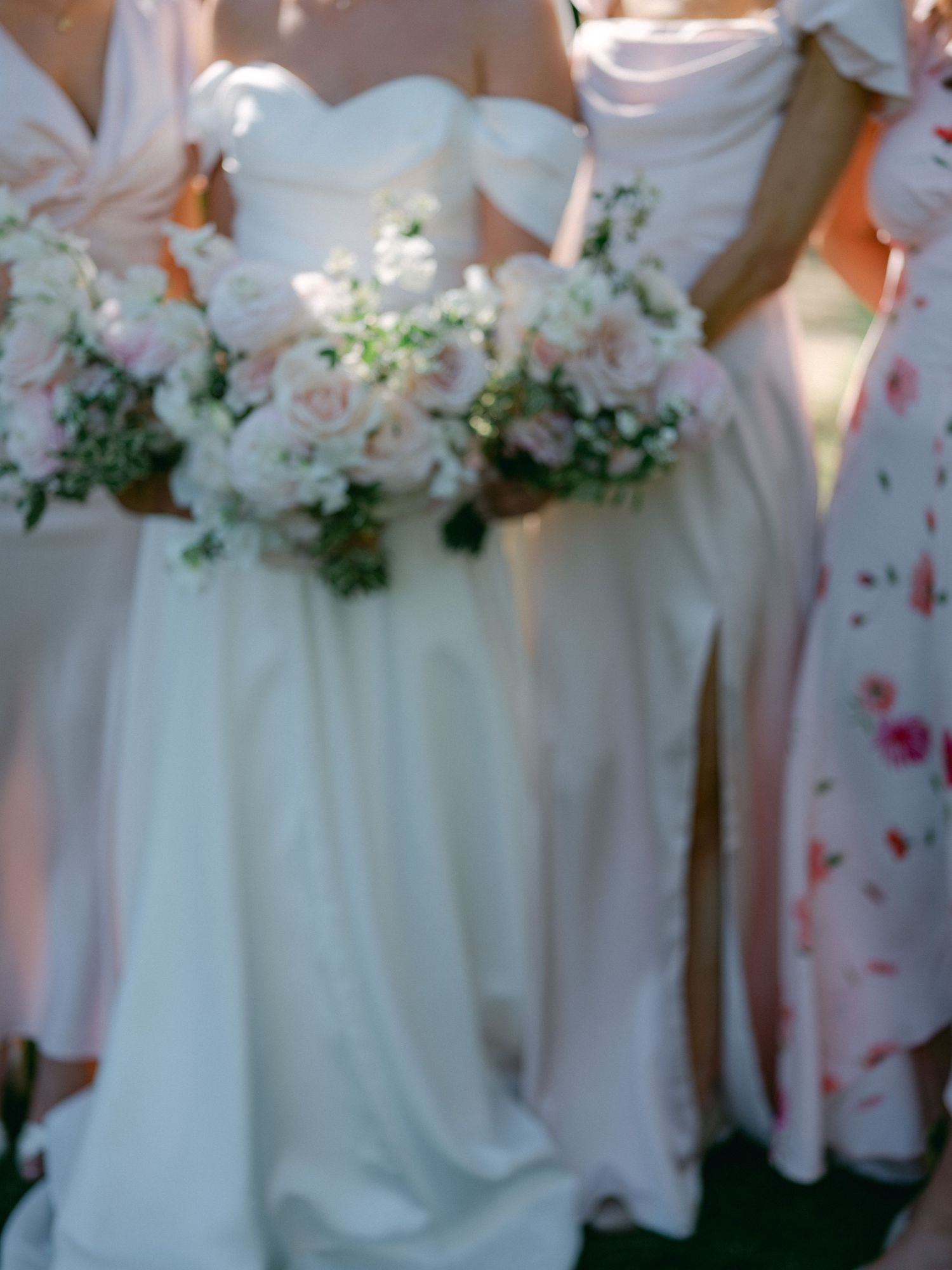Bride and bridesmaids holding lush blush pink and white floral bouquets in elegant white and floral gowns.