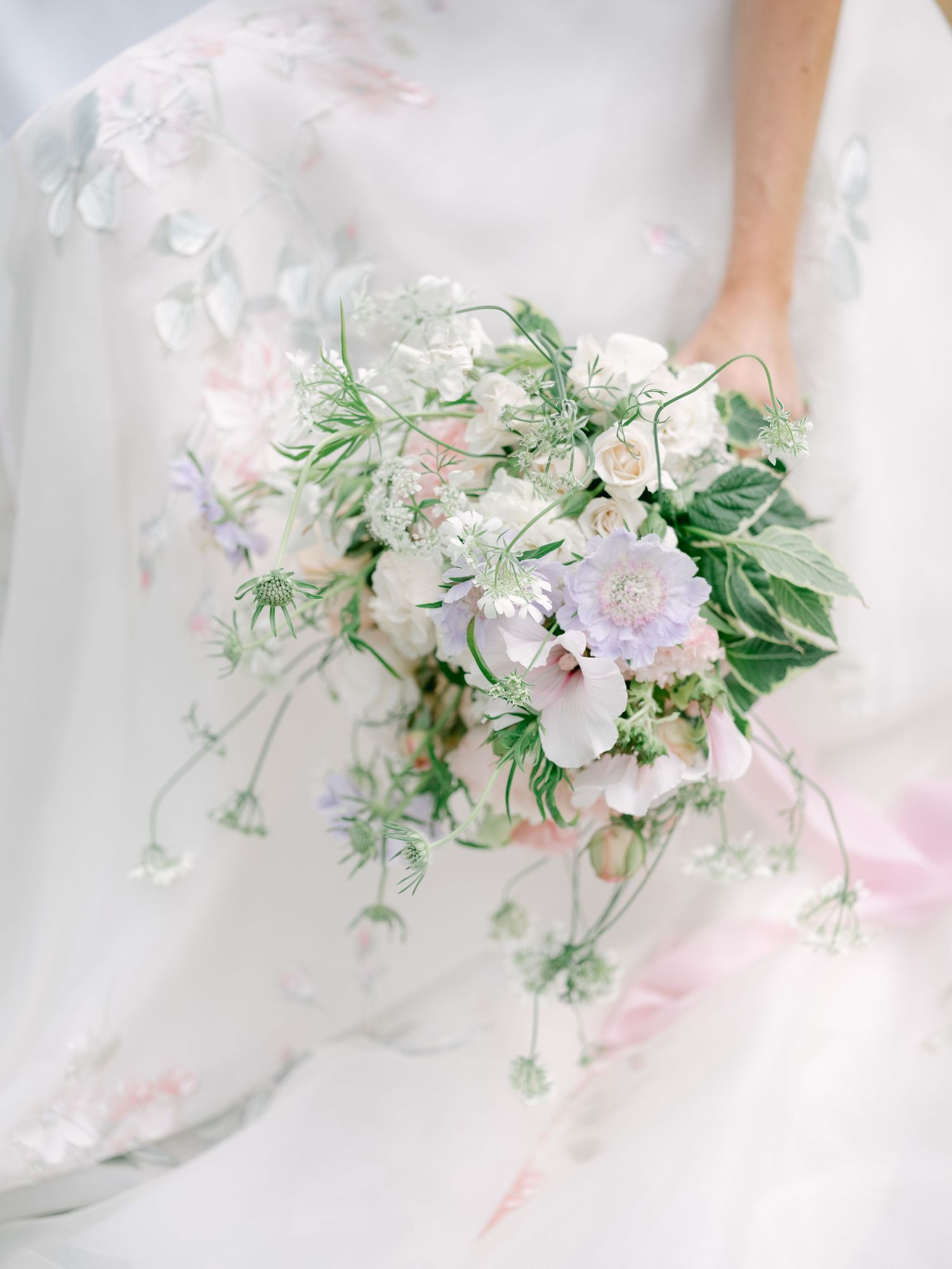 Delicate pastel wedding bouquet featuring soft pink roses and cascading greenery with ethereal styling and light airy composition.