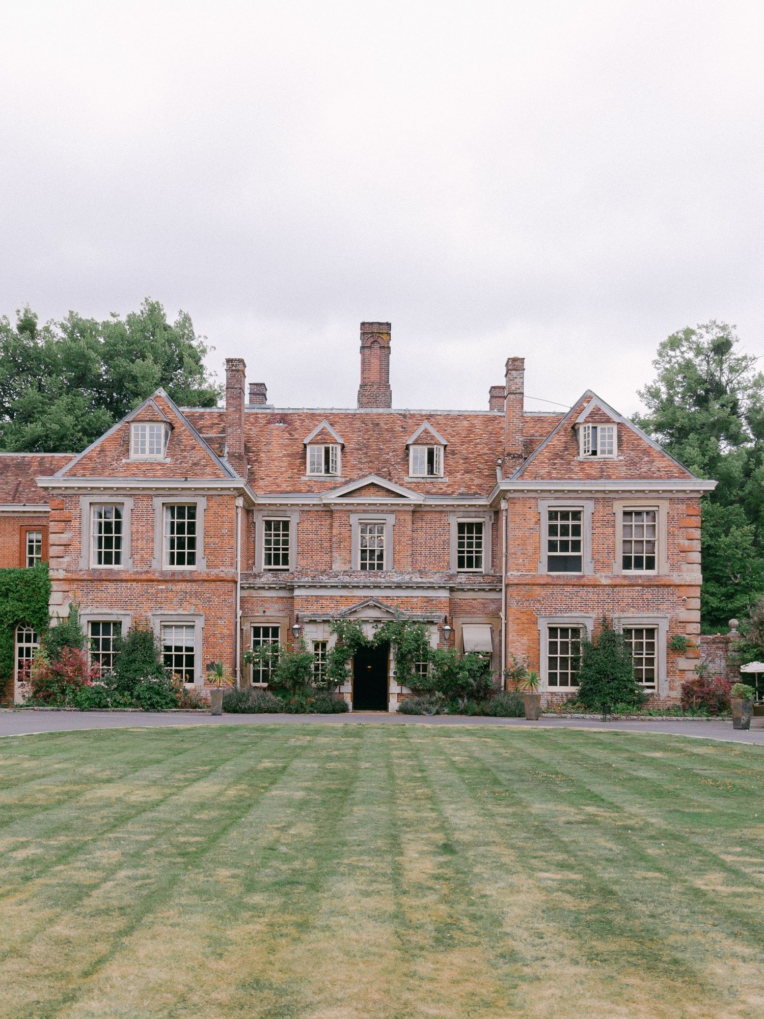 Historic red brick manor house with dormer windows and multiple chimneys viewed from different angles across a manicured lawn.