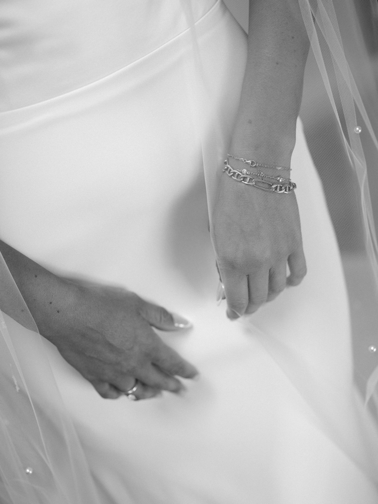 Close-up black and white photo of hands delicately holding the fabric of a wedding dress with intricate beading details.