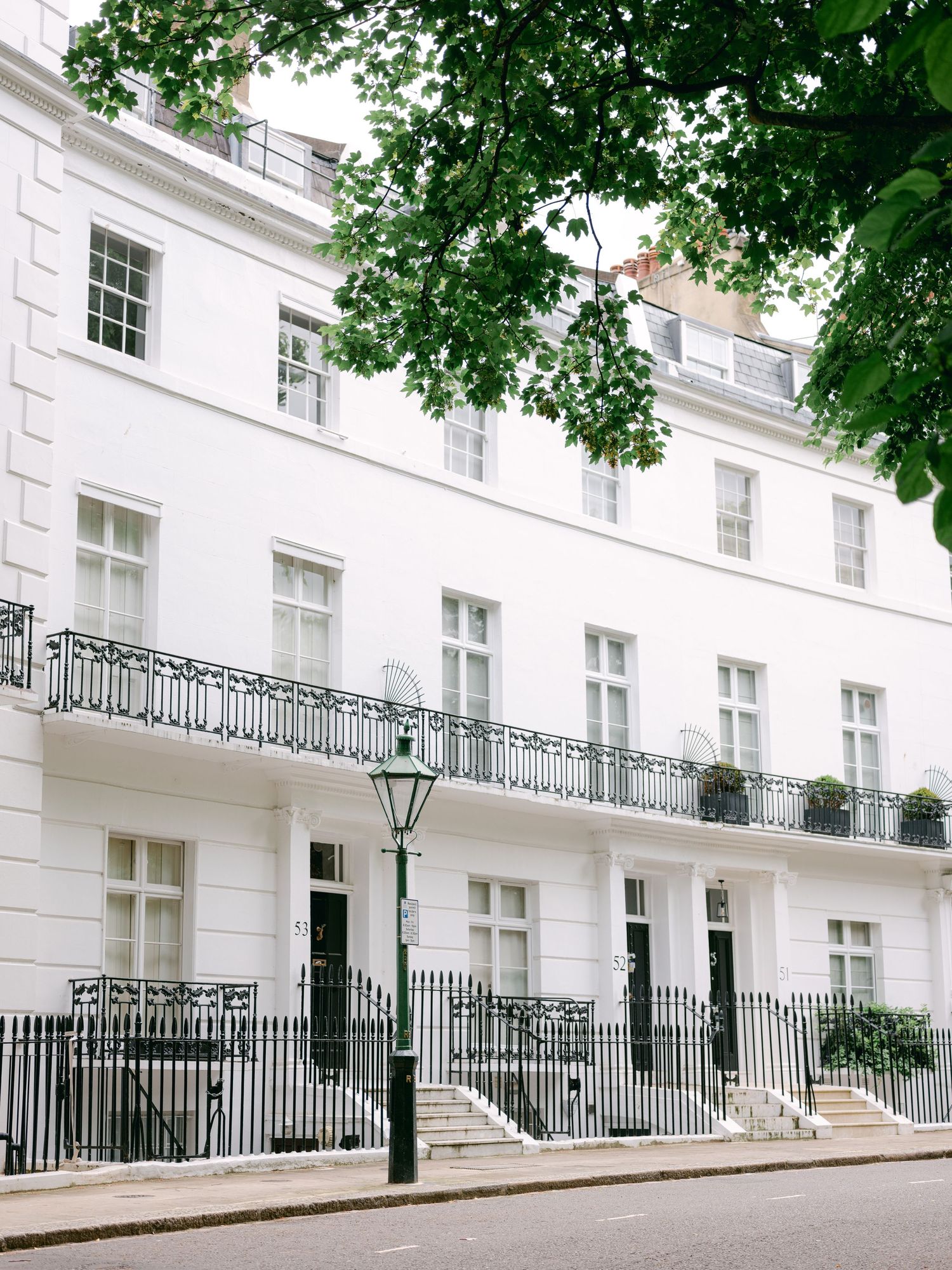 Row of elegant white Georgian townhouses with black railings and street lamp on a curved residential street in London.