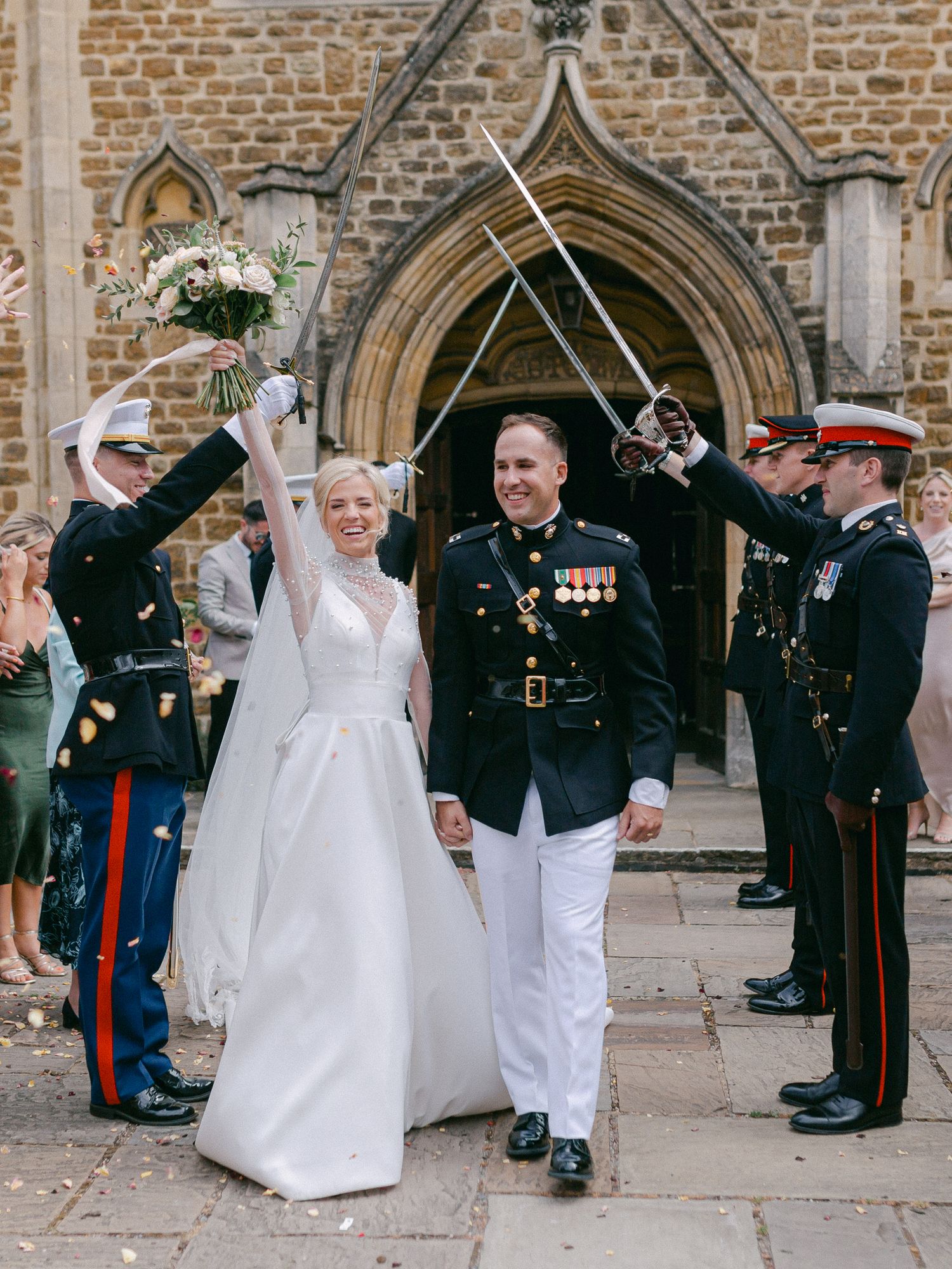 Military wedding ceremony outside historic stone church with sword arch salute and traditional dress uniforms.