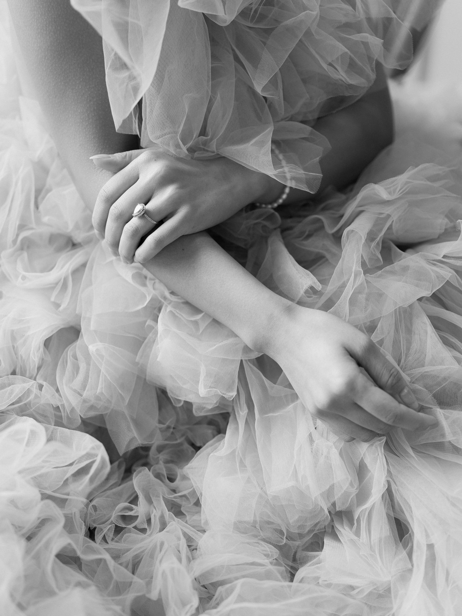 Black and white photo of a bride in a ruffled tulle gown, hands folded showing an elegant engagement ring.