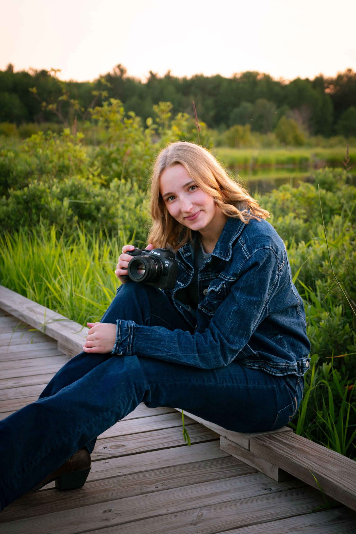 Person in denim jacket relaxing on wooden boardwalk surrounded by green marsh grass.