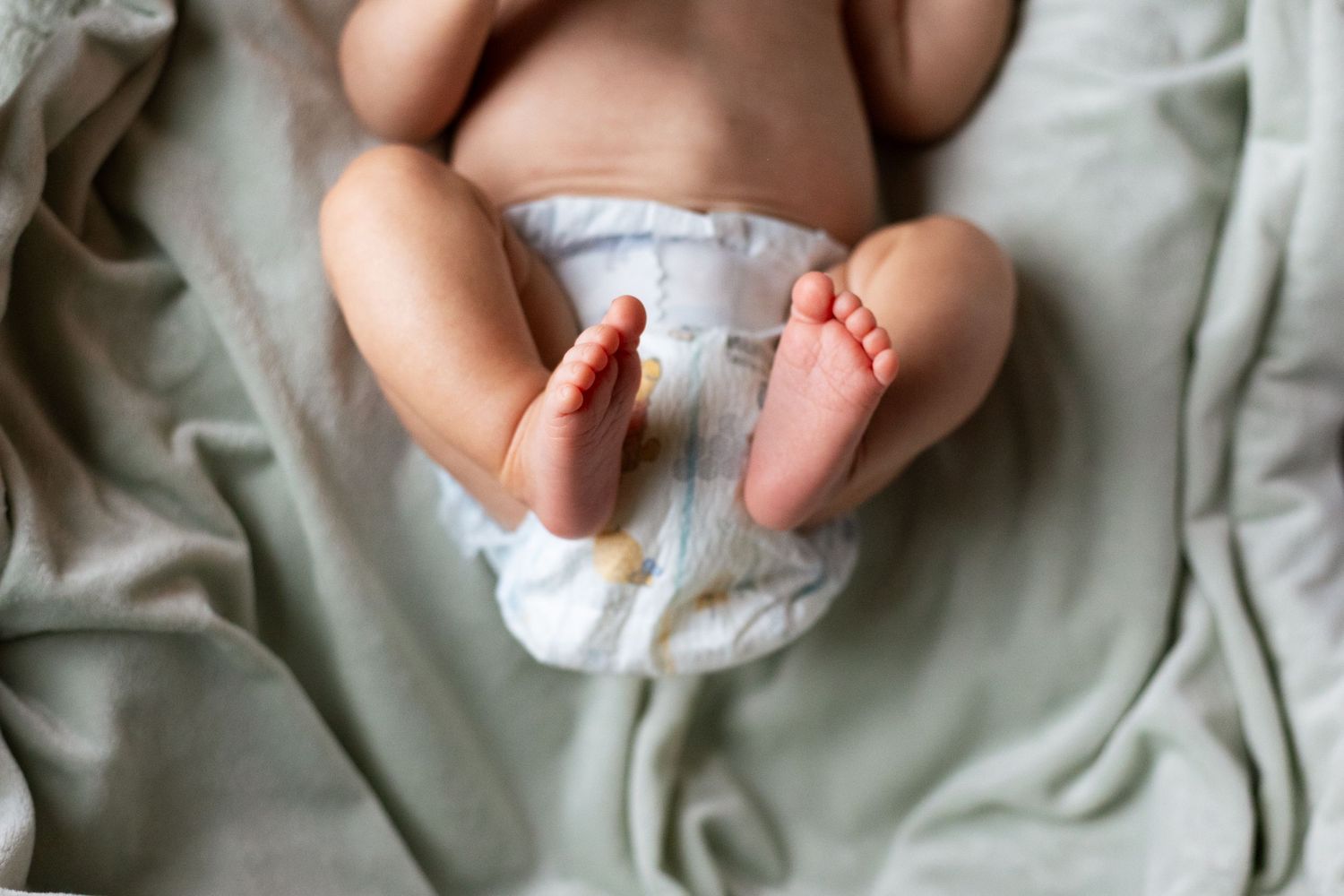 Newborn baby wrapped in soft white blanket lying on grey fabric.