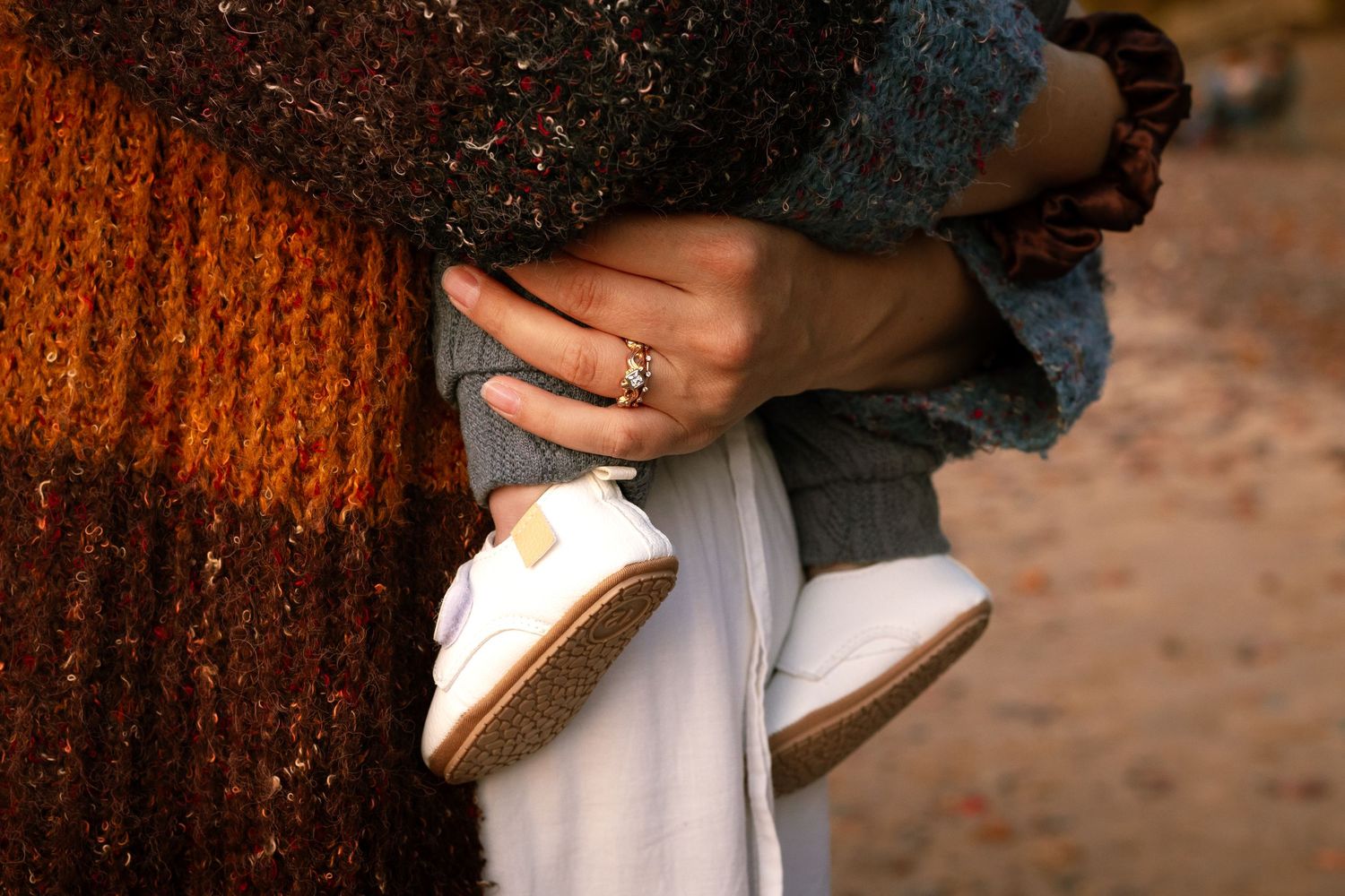 A couple holds hands wearing wedding rings against a rustic wooden background in warm lighting.
