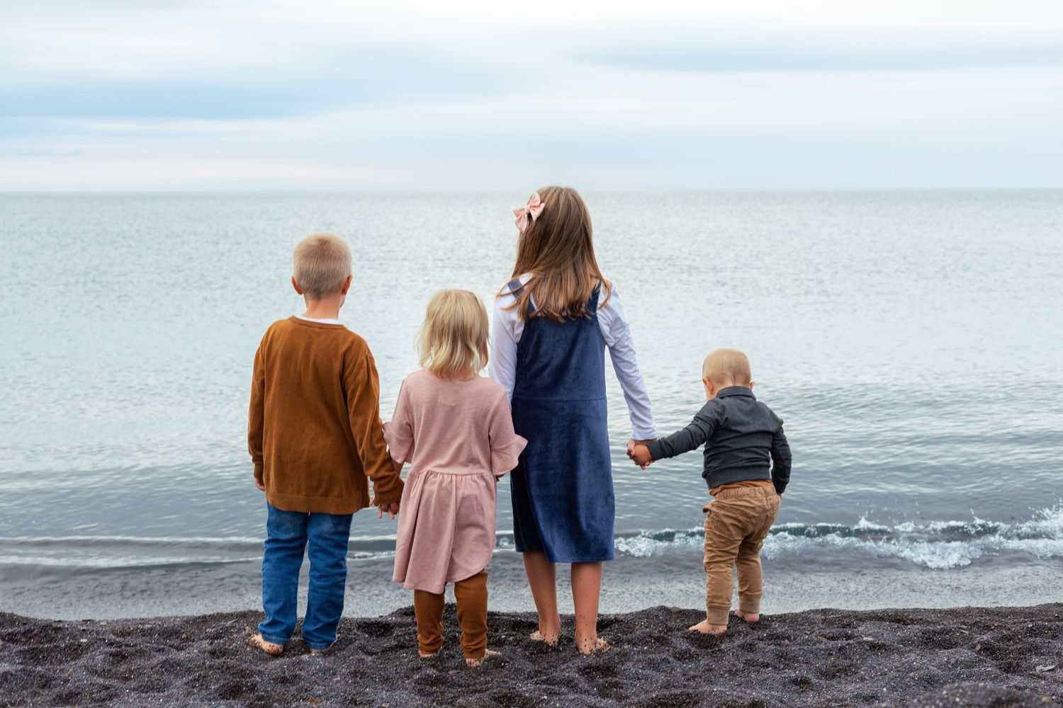 Four people sit together on a rocky beach looking out at the ocean and waves on an overcast day.