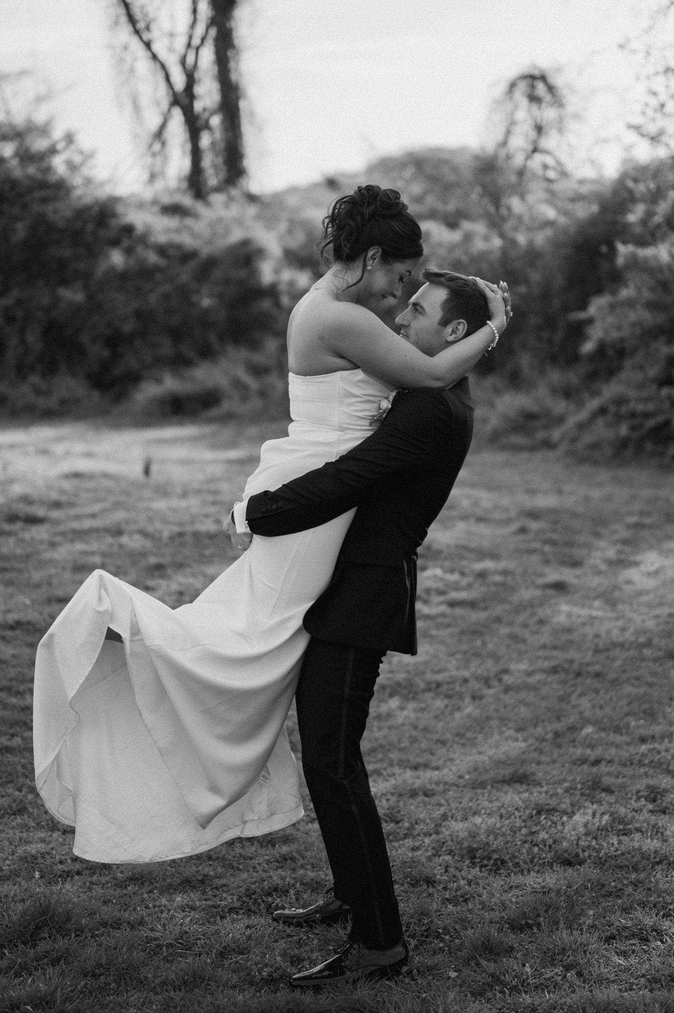 A romantic black and white wedding photo showing a couple embracing outdoors, with the bride's dress flowing in the breeze.