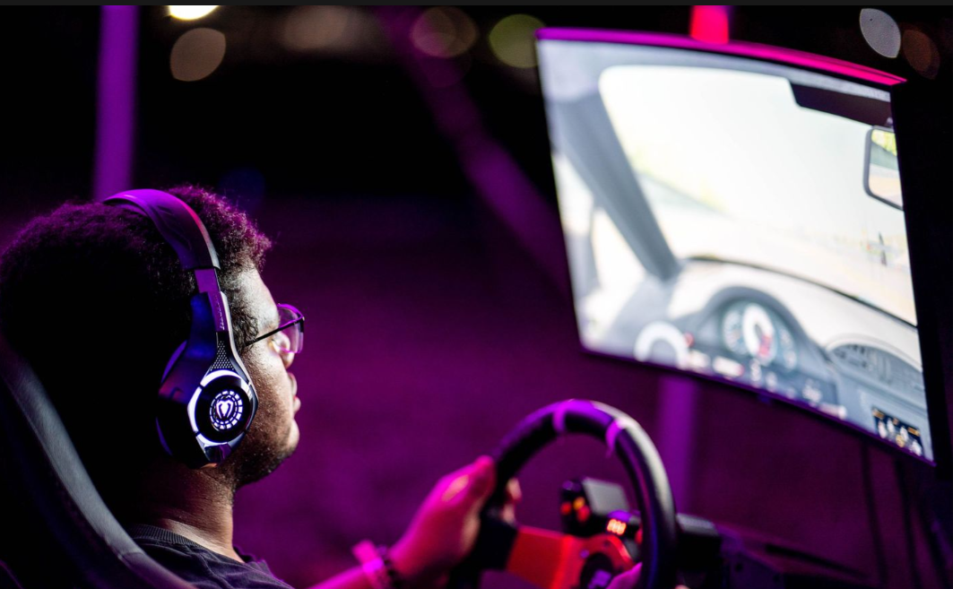 Man wearing headphones plays a racing video game simulator with steering wheel under purple ambient lighting.