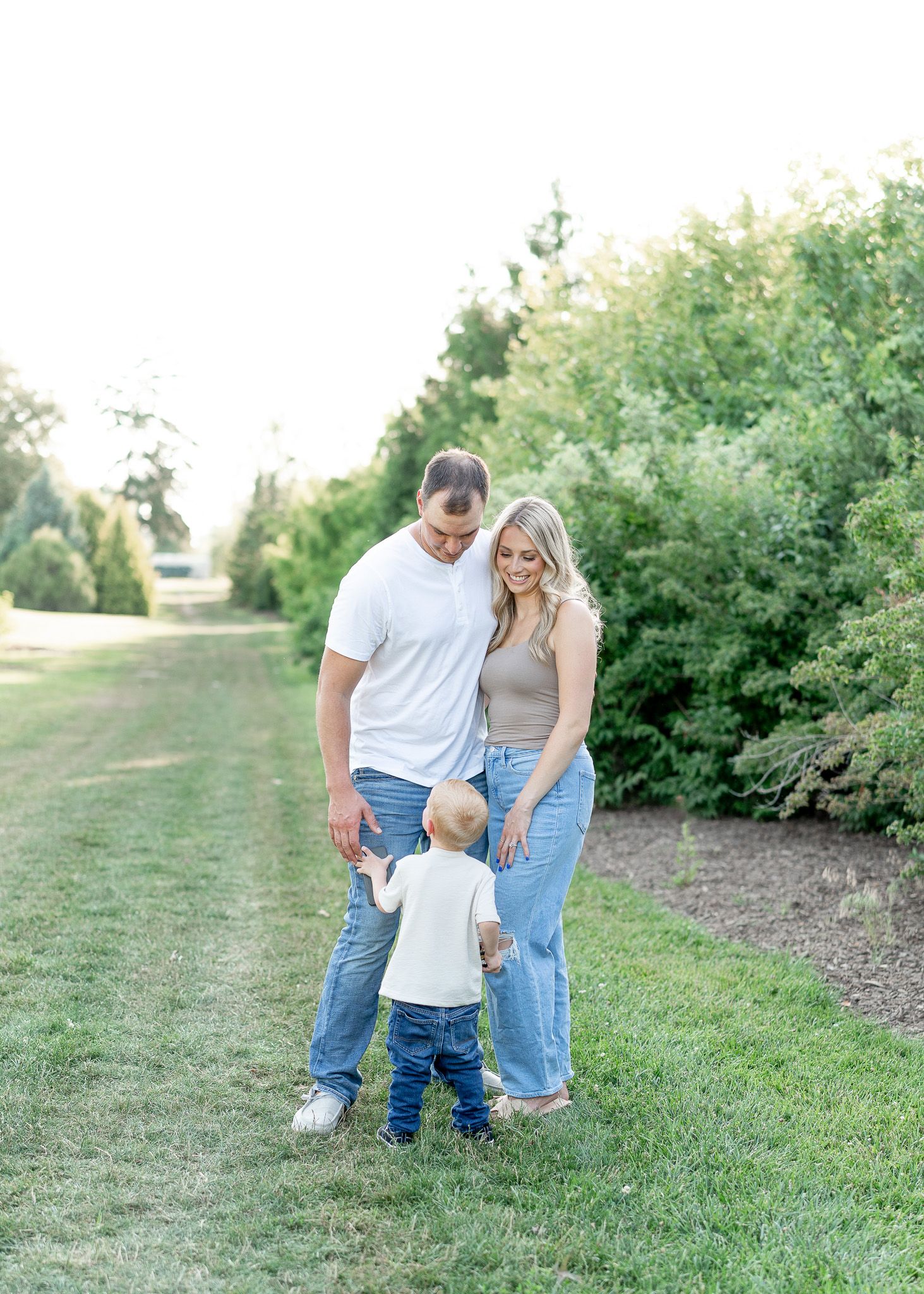 A family in casual attire walks together on a grassy path during a sunny outdoor photo session.
