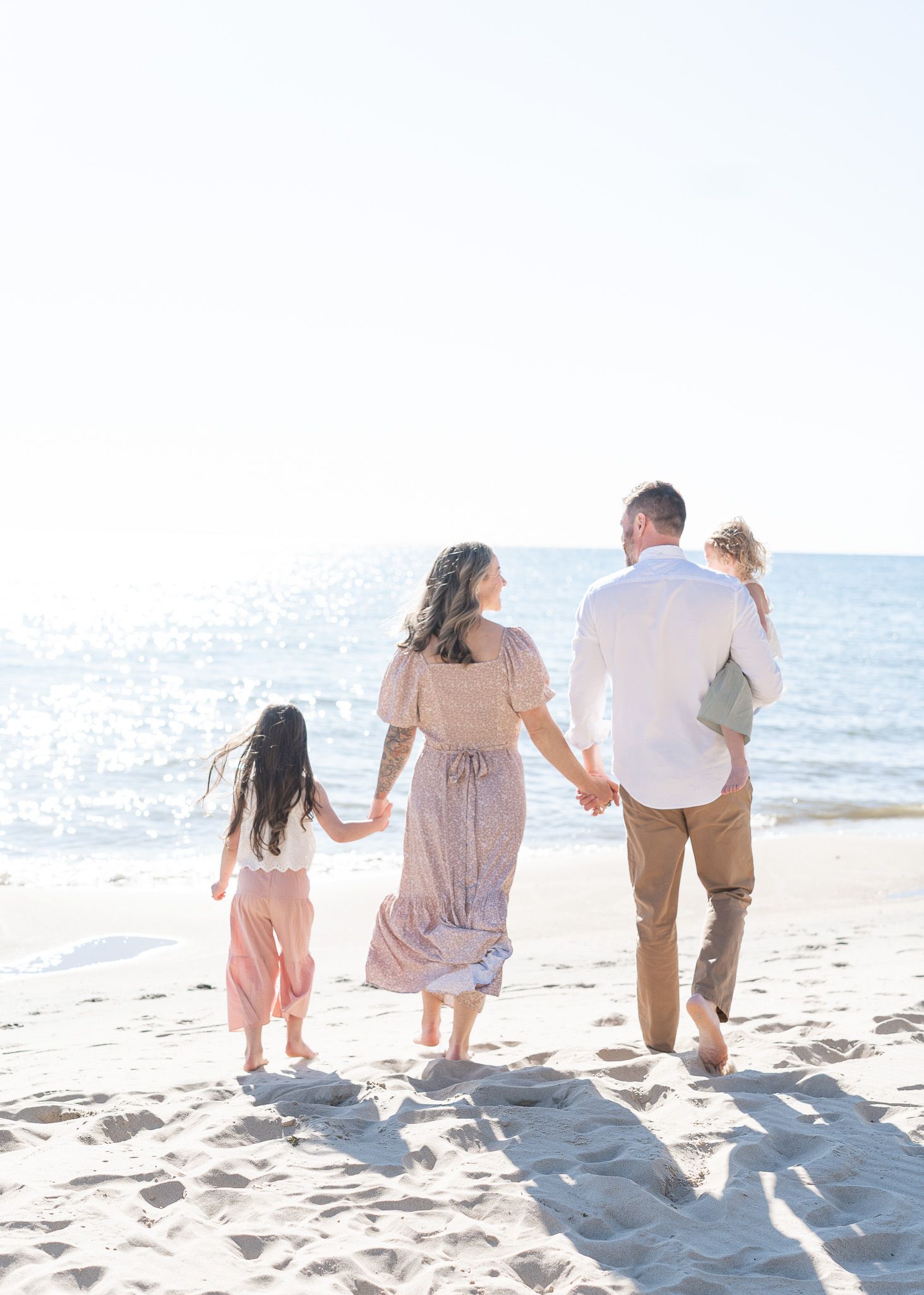 Group walking together along a sunny beach shoreline with waves and sand visible in the background.